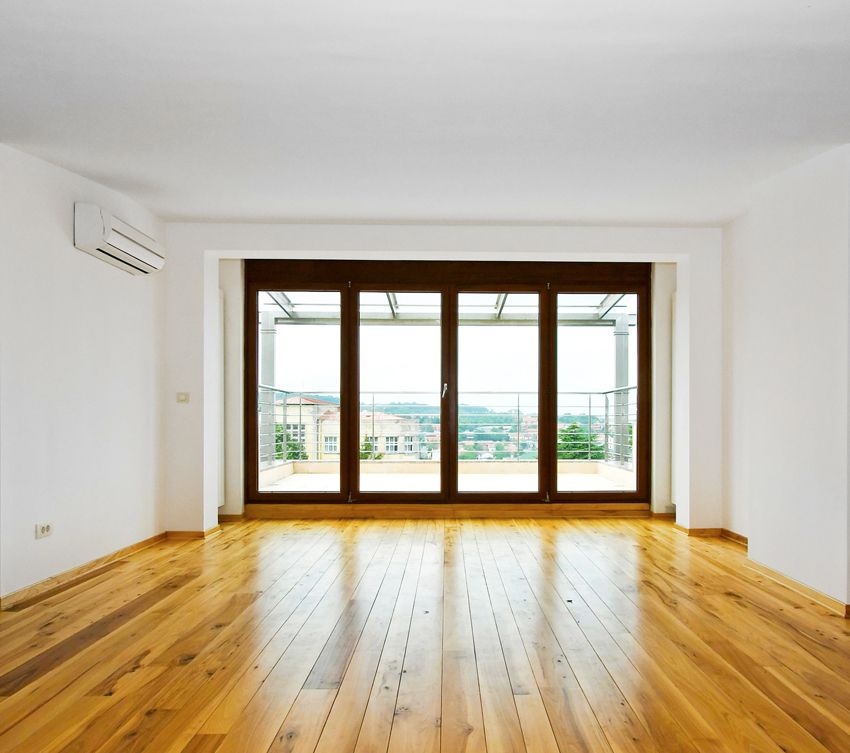 Empty room with wooden floors, large glass doors to a balcony, white walls, and an air conditioner.