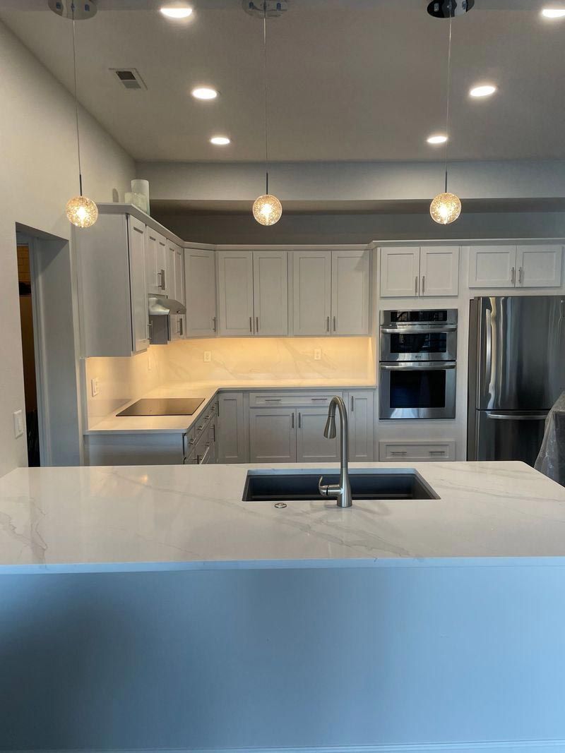 A kitchen with white cabinets , stainless steel appliances , a sink , and a large island.