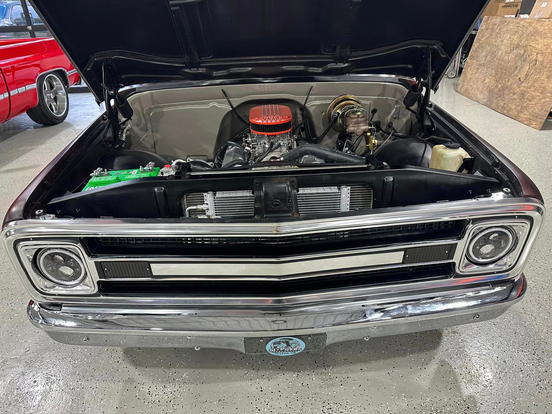 A black truck with the hood up is parked in a garage.