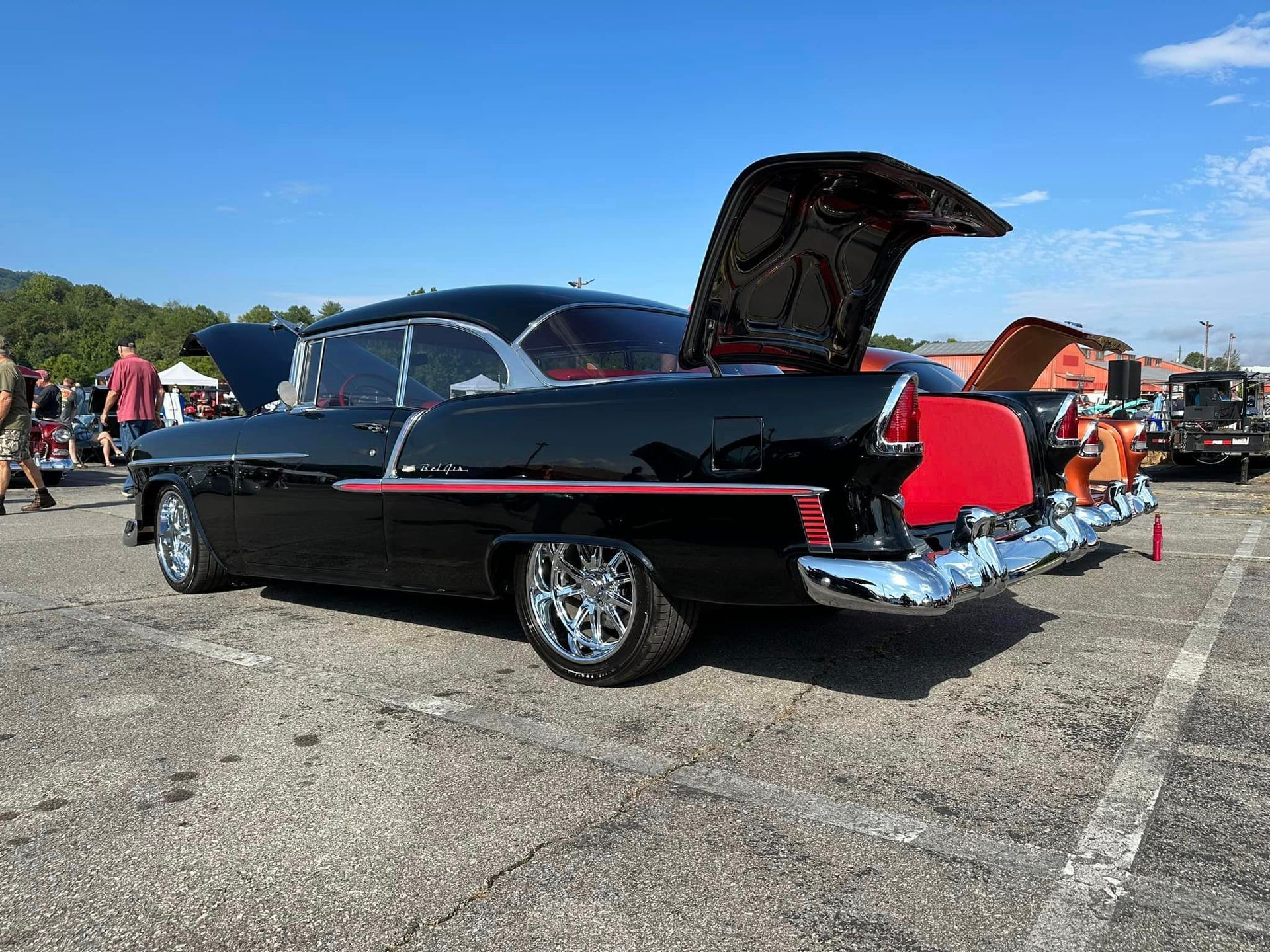 A black car with the hood up is parked in a parking lot.
