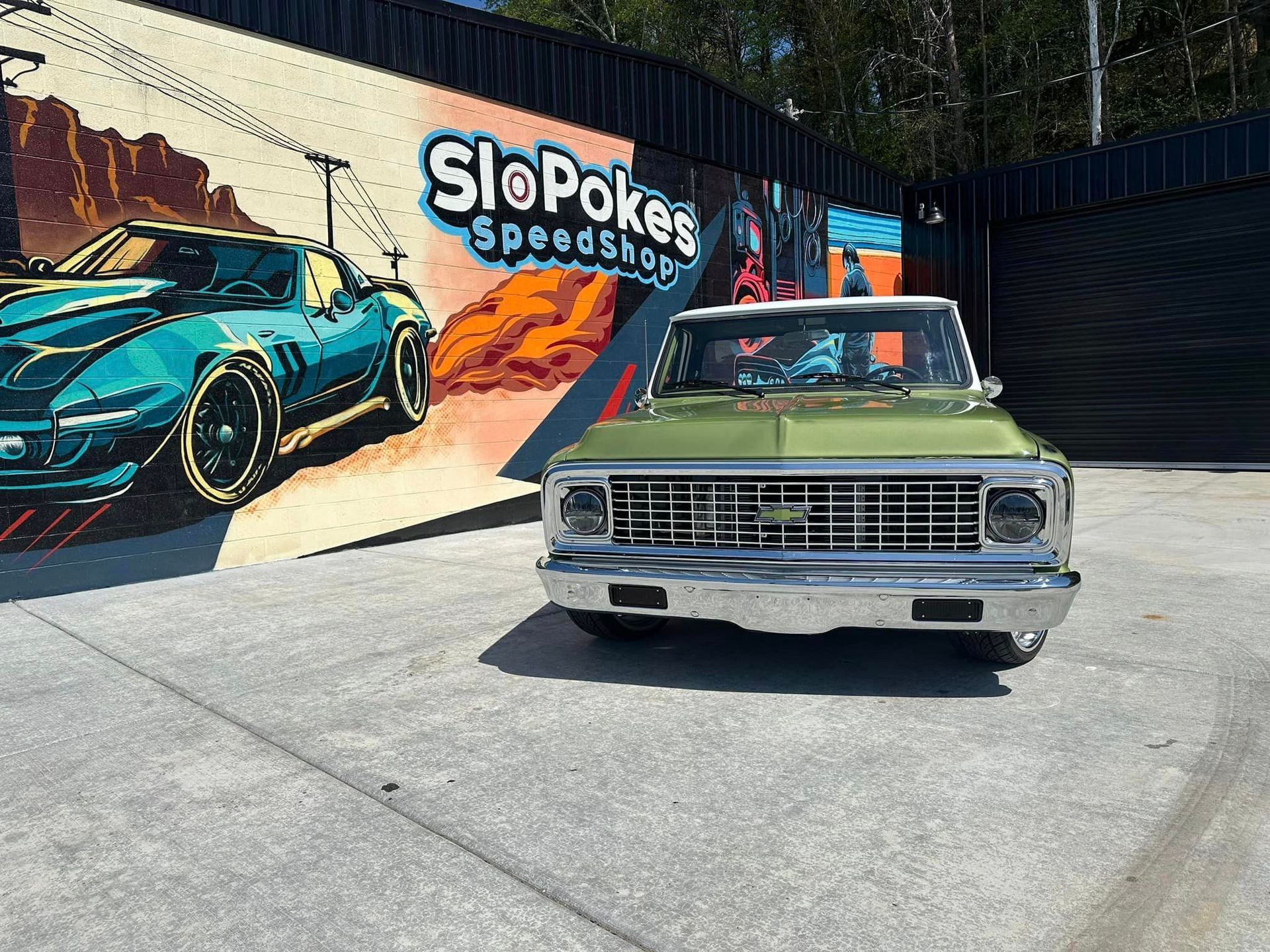 A green car is parked in front of a speed shop.