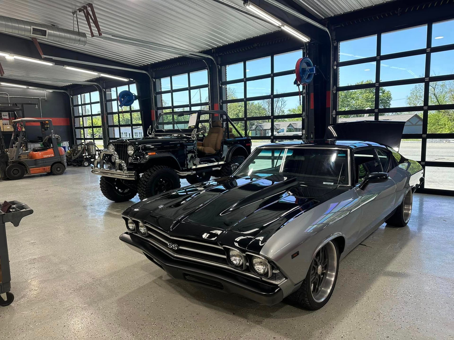 A black car is parked in a garage next to a jeep.
