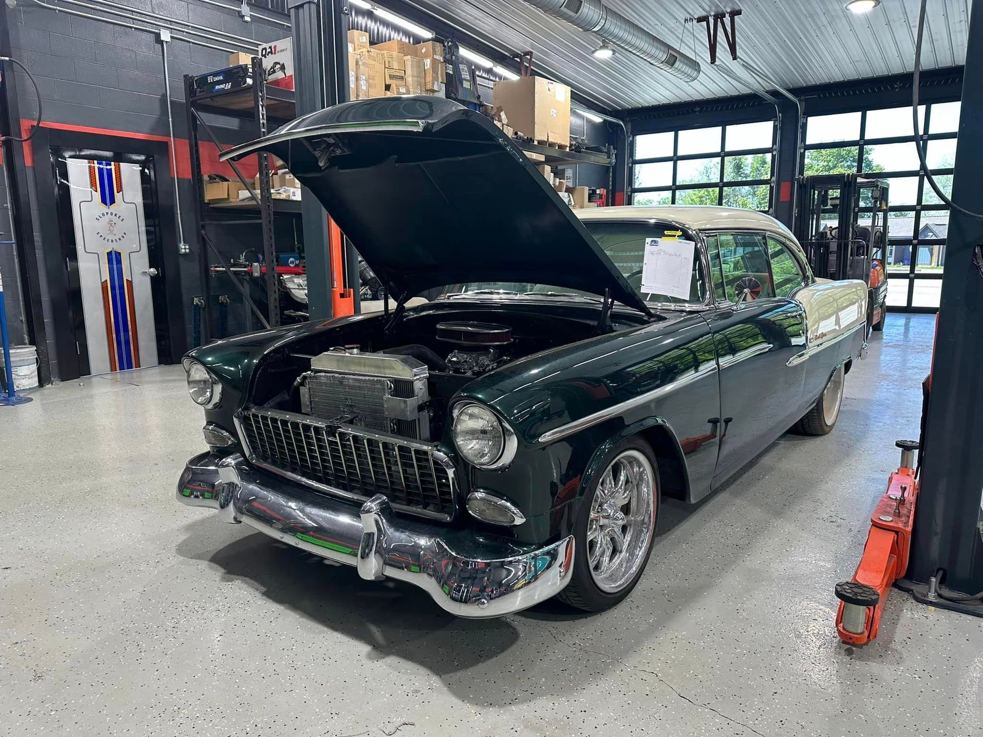 A green car with the hood up is parked in a garage.