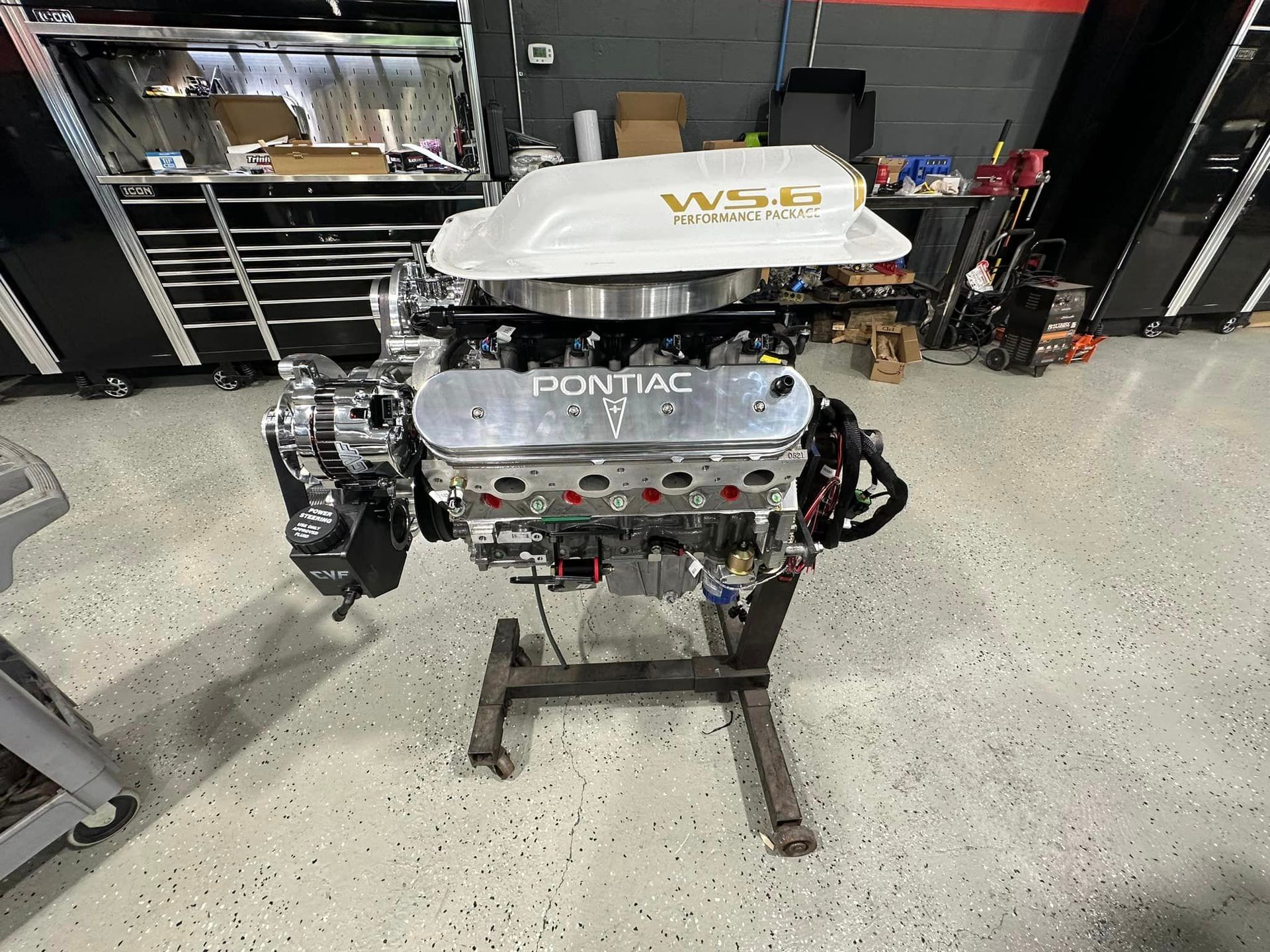 A pontiac engine is sitting on a stand in a garage.