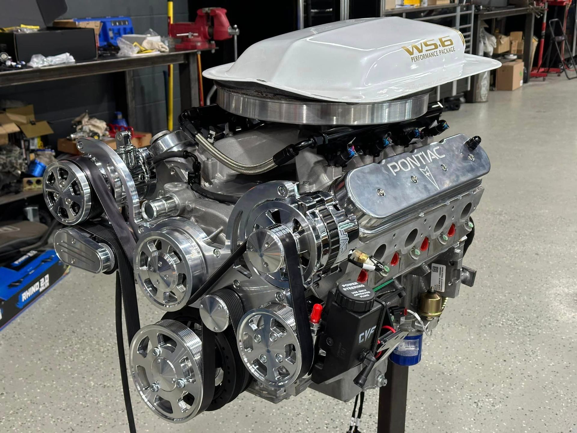 A pontiac engine is sitting on a stand in a garage.