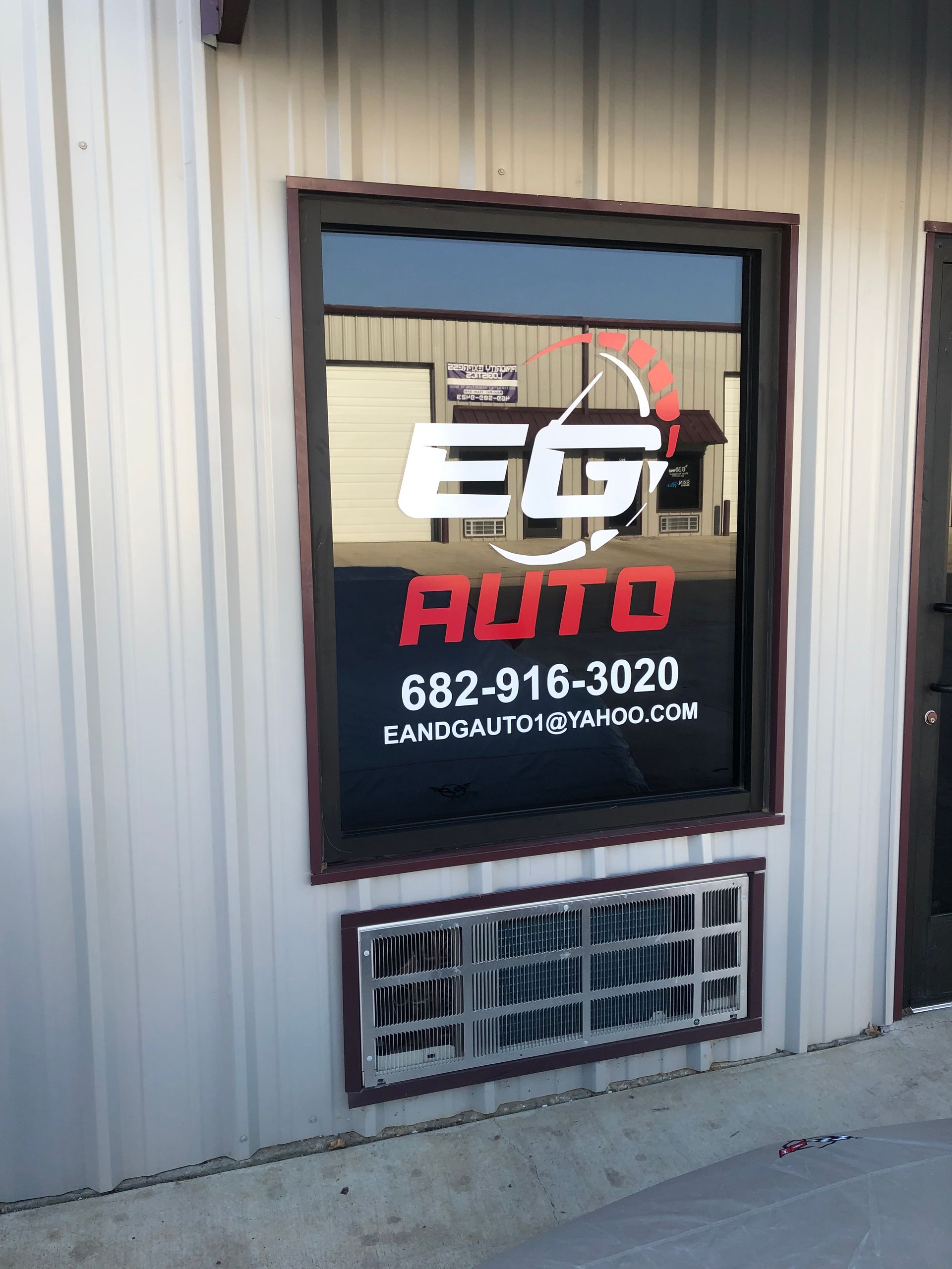 EG Auto shop window sign on a beige metal building, with phone number and a red logo.