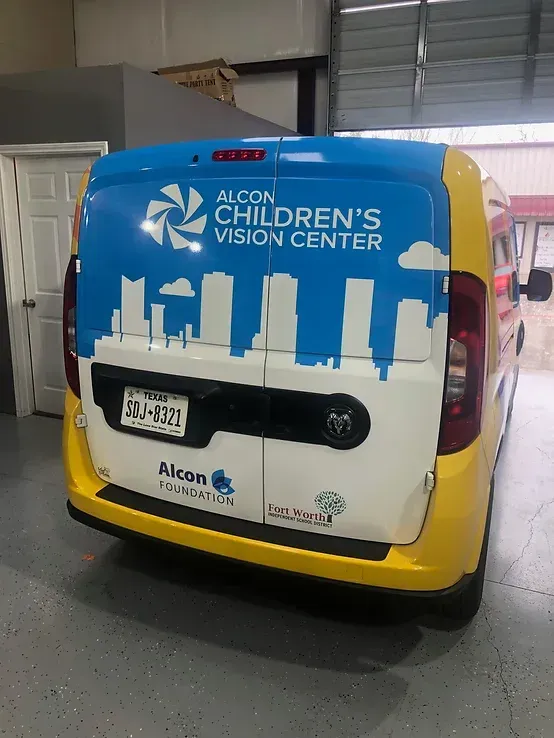 Blue-and-white Children’s Vision Center van with skyline graphic, parked indoors.