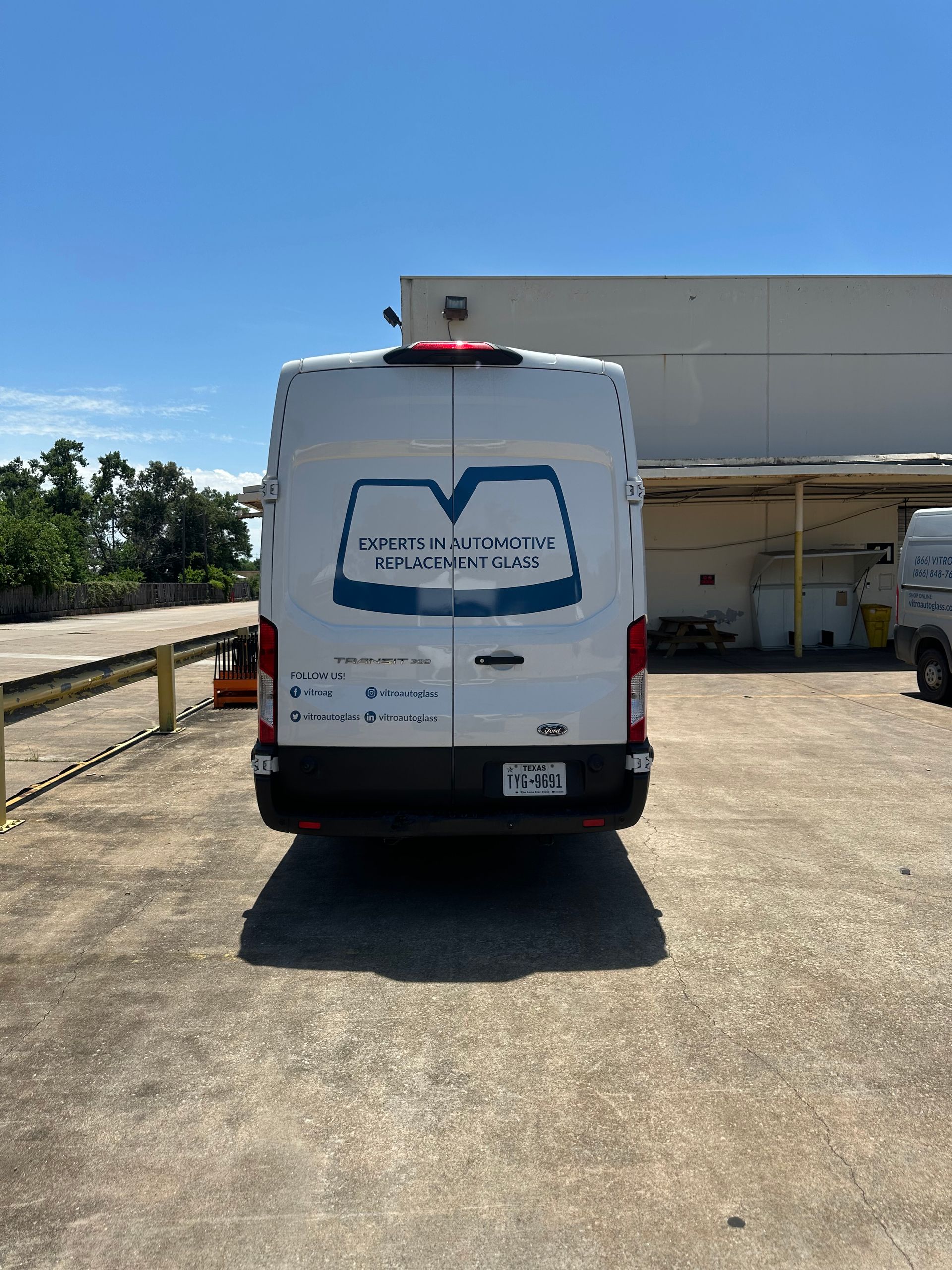 White delivery van parked in an industrial lot beside a warehouse under a clear blue sky