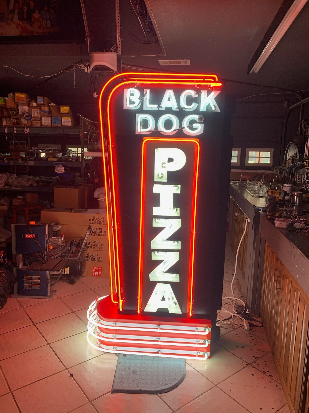 Neon sign reading “BLACK DOG PIZZA” glowing red and white in a dim restaurant interior