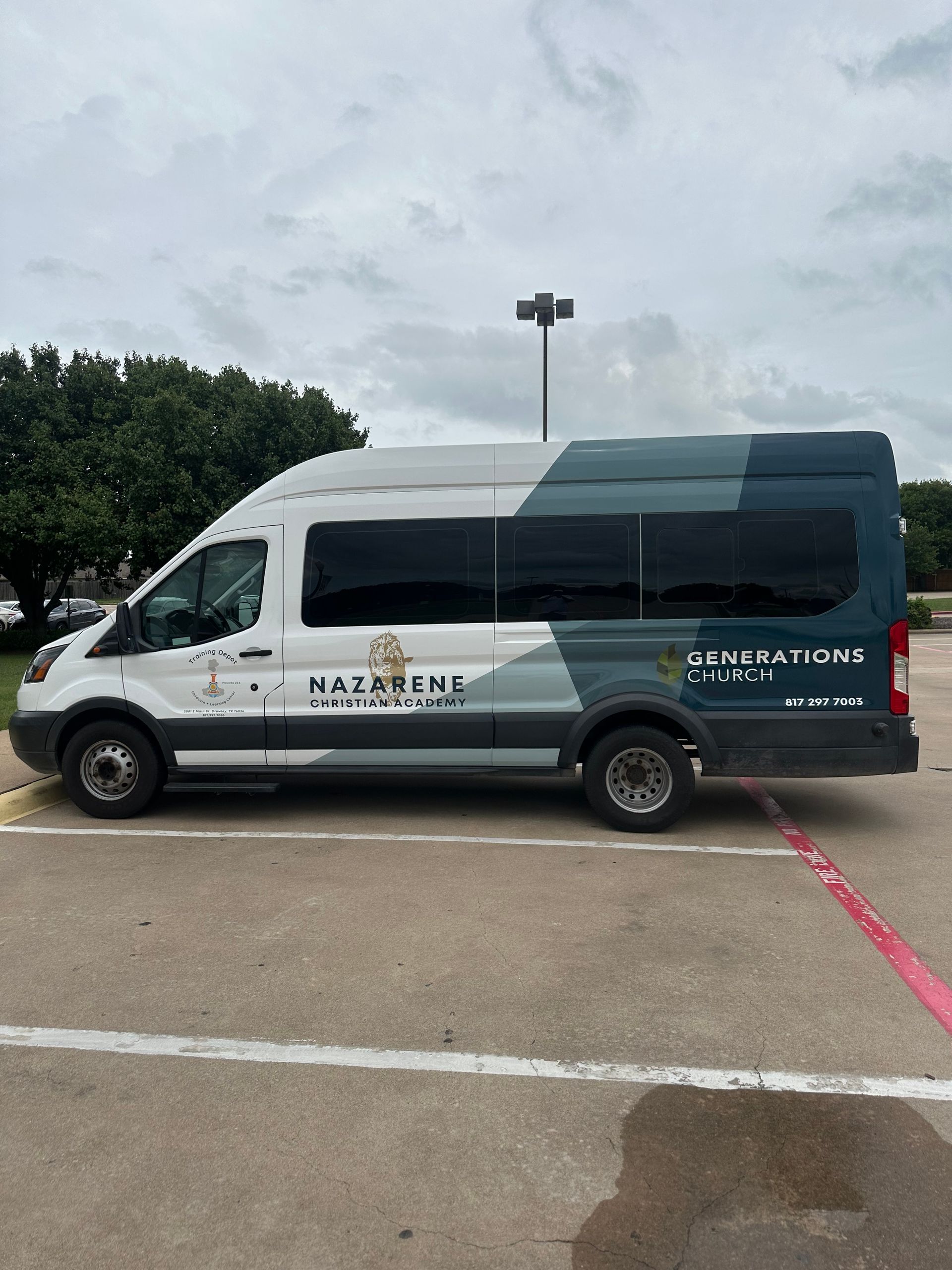 White shuttle van with company branding parked in a lot under a cloudy sky.