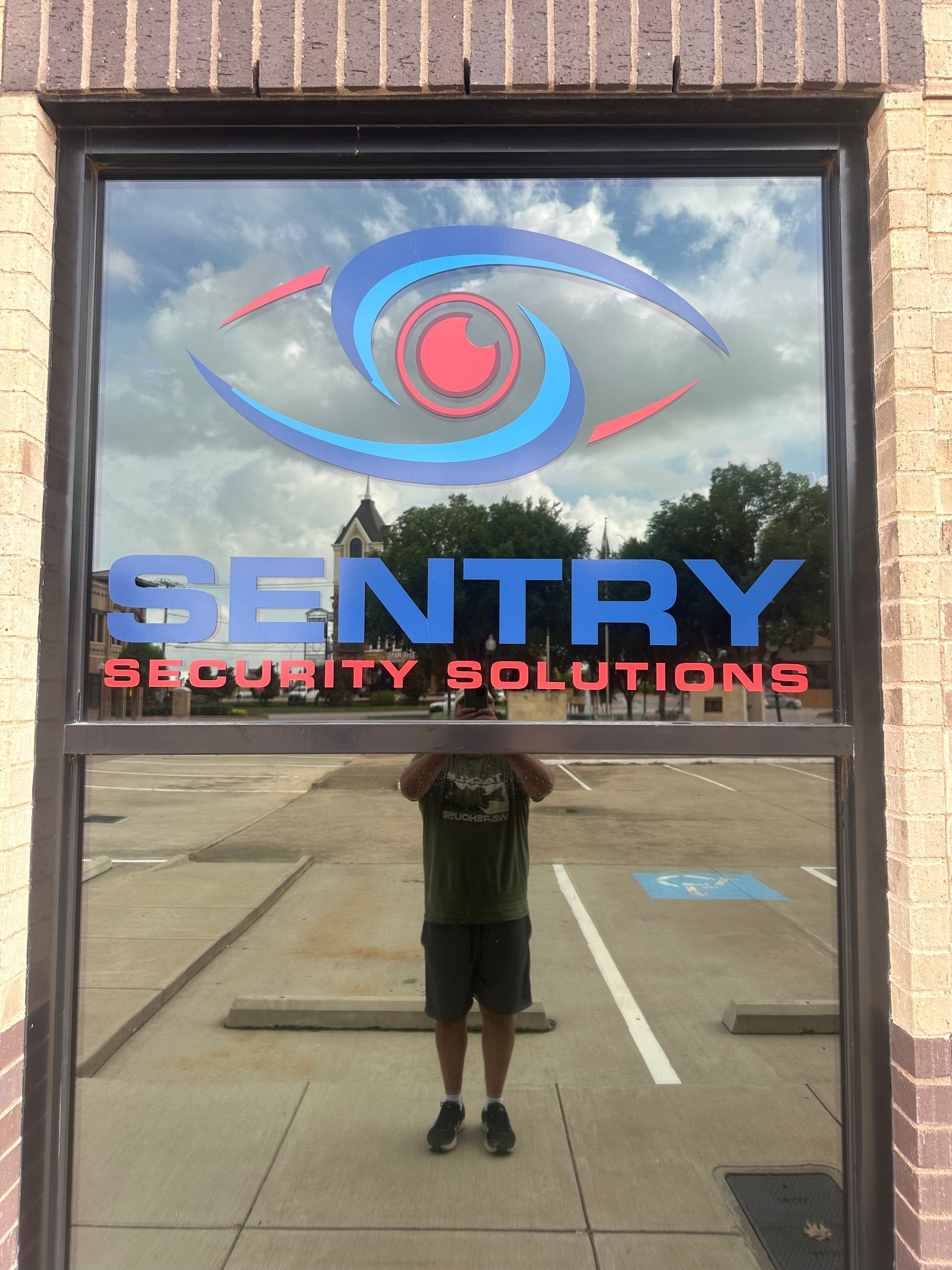 Sentry Security Solutions storefront sign reflected in glass, with blue and red logo and text.