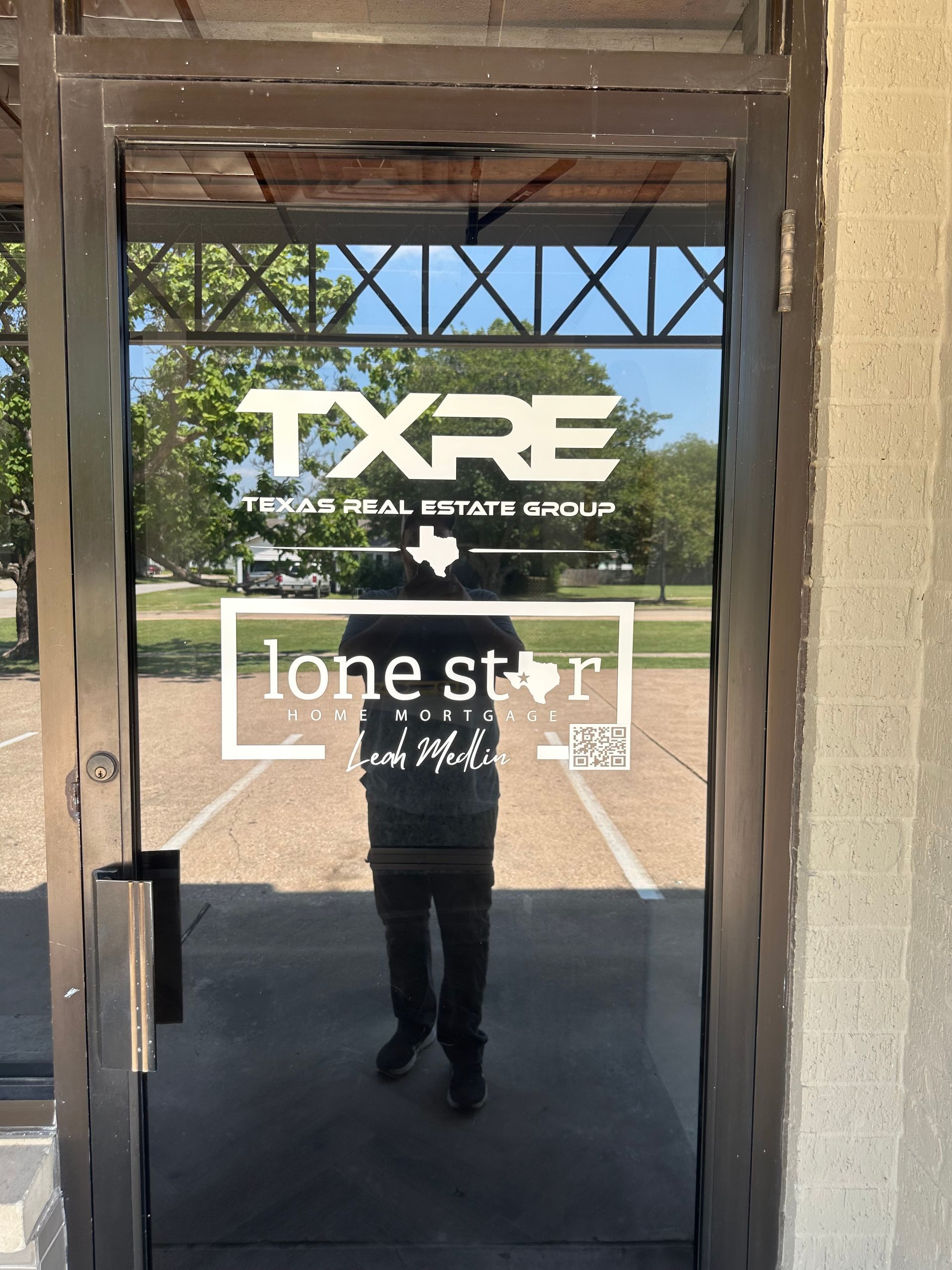 Glass door with TXRE and Lone Star logos, reflecting a person standing outside a storefront.