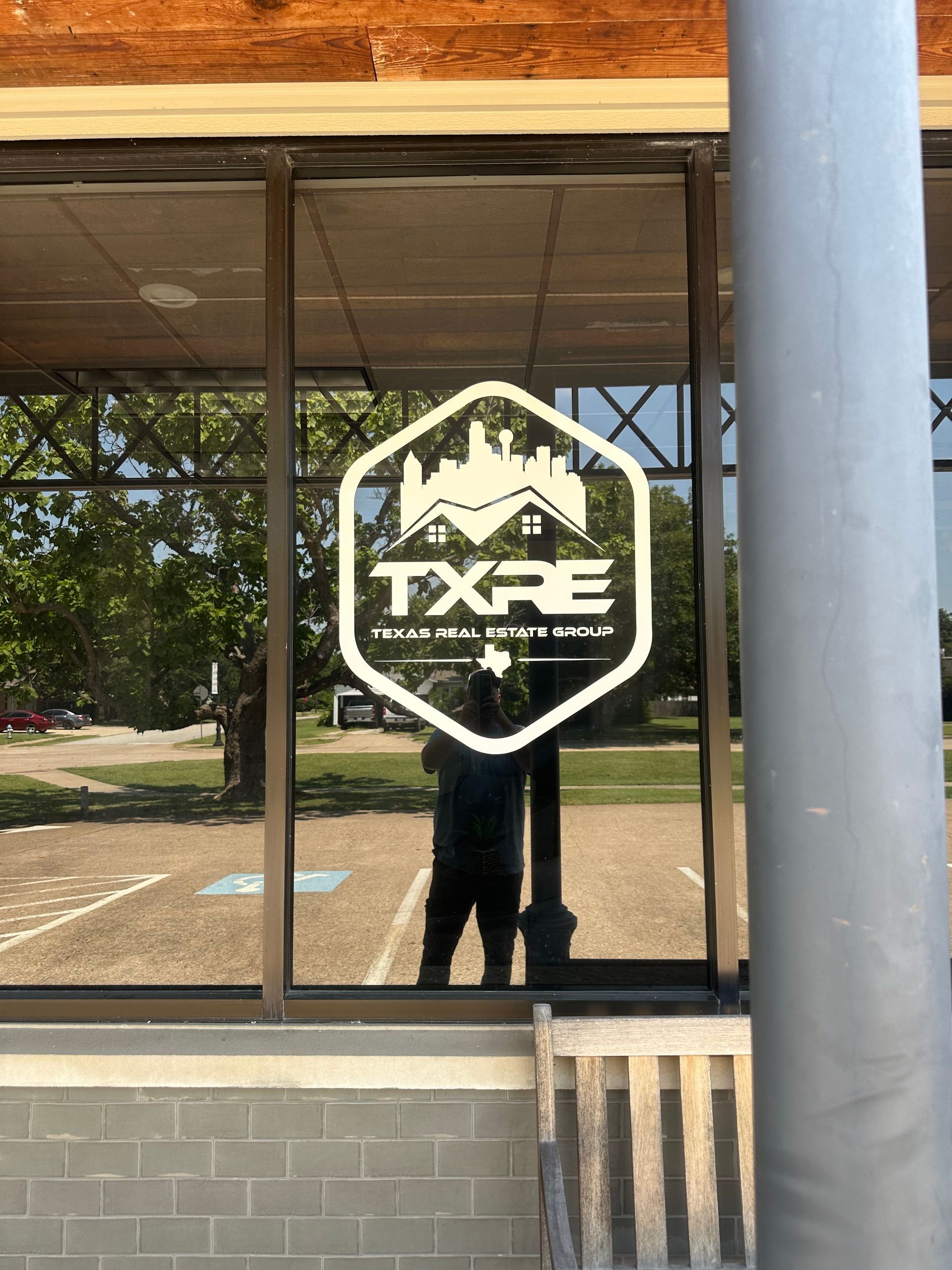TXF logo on a glass storefront with reflections and a gray pillar in front
