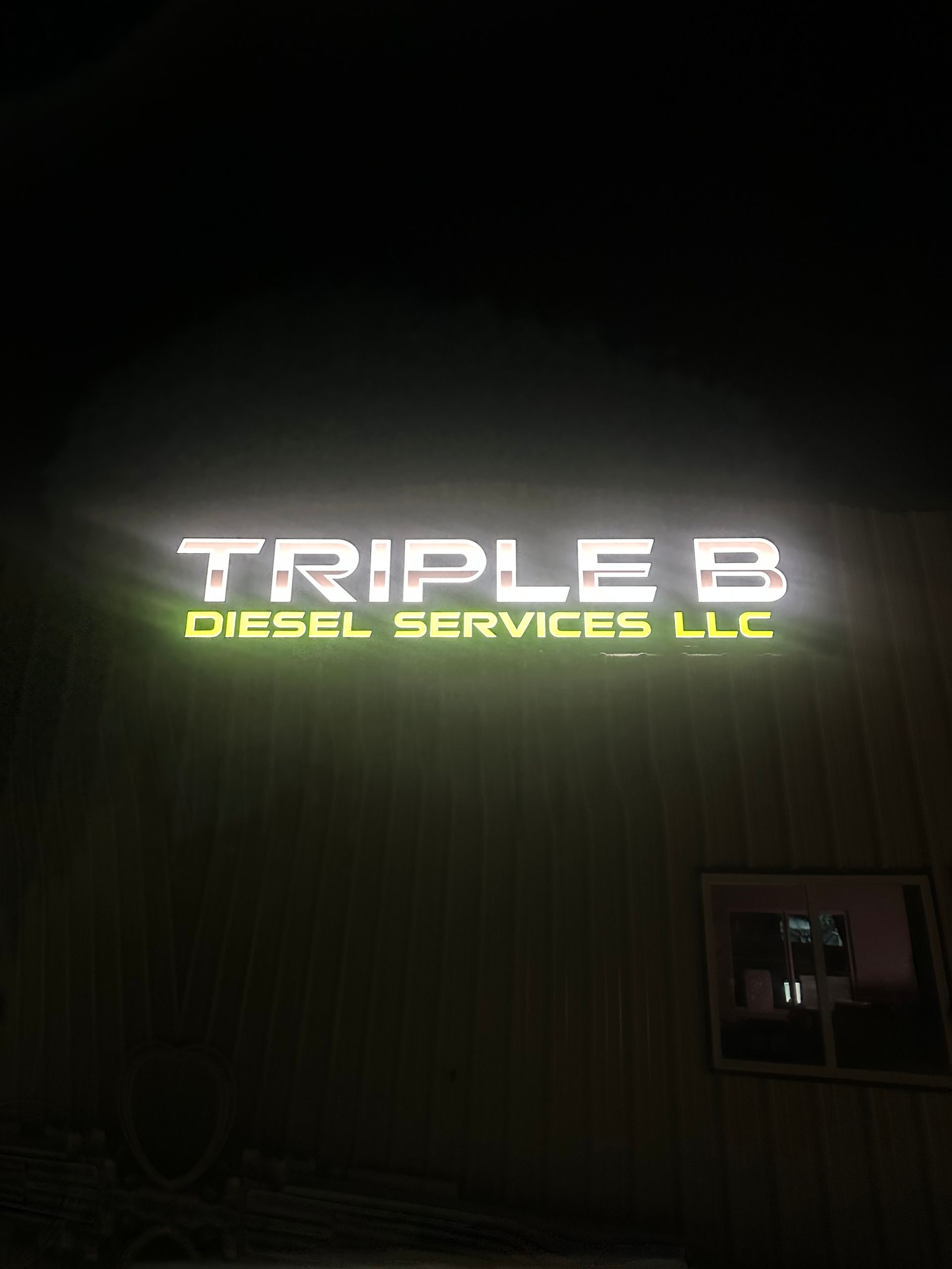 Illuminated “Triple B Diesel Services LLC” sign on a dark building exterior