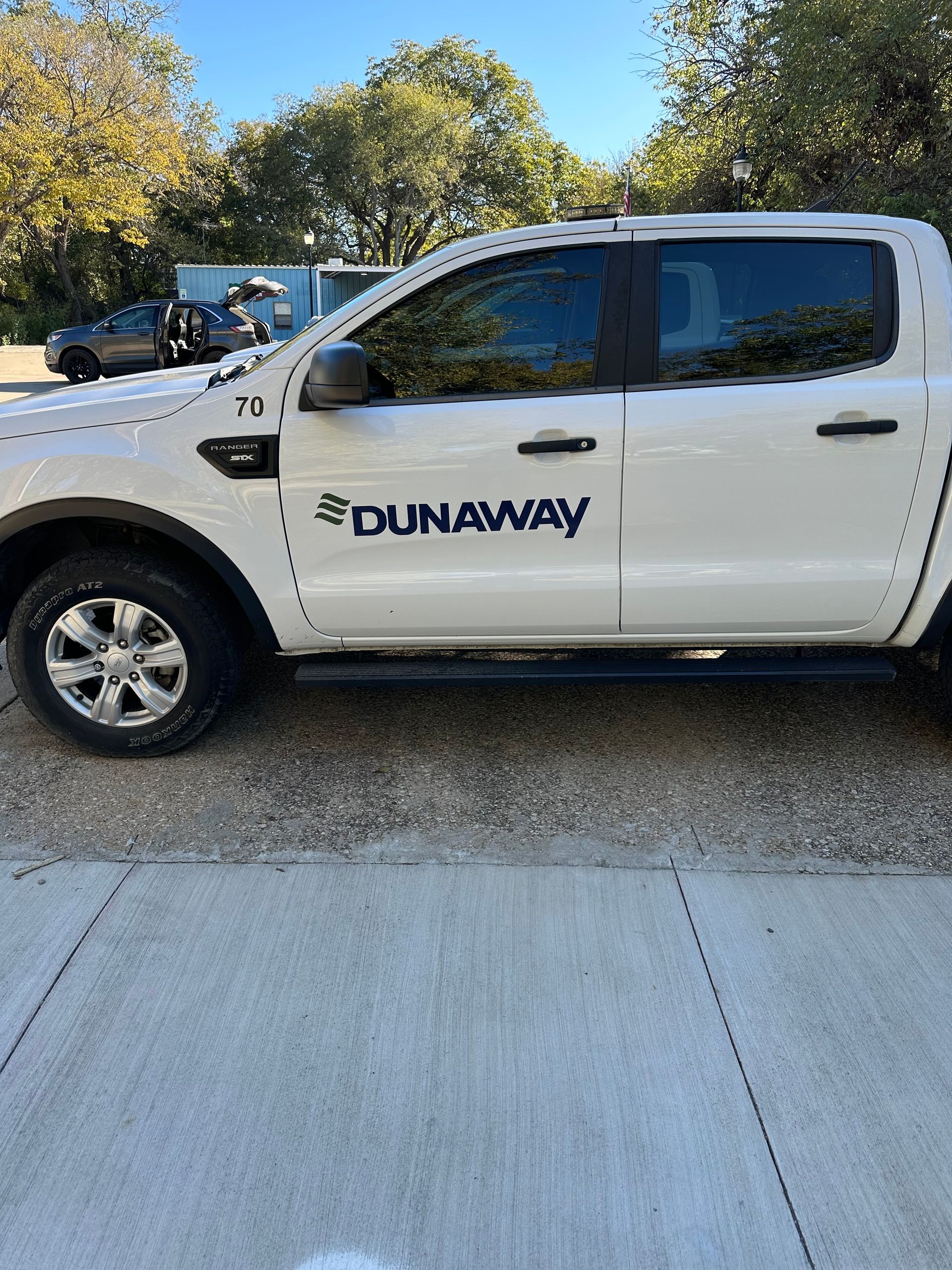 White Dunaway pickup truck parked outdoors beside a sidewalk and trees.