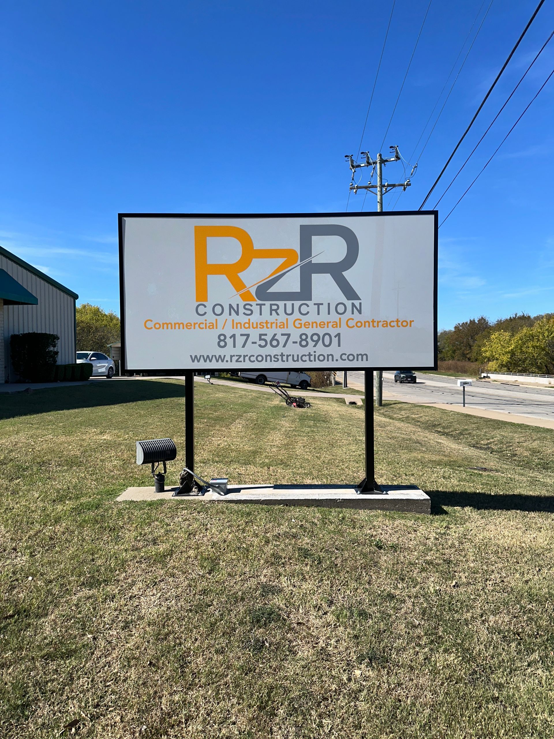 R2R Construction sign on a grassy lot under a blue sky, with utility lines overhead.