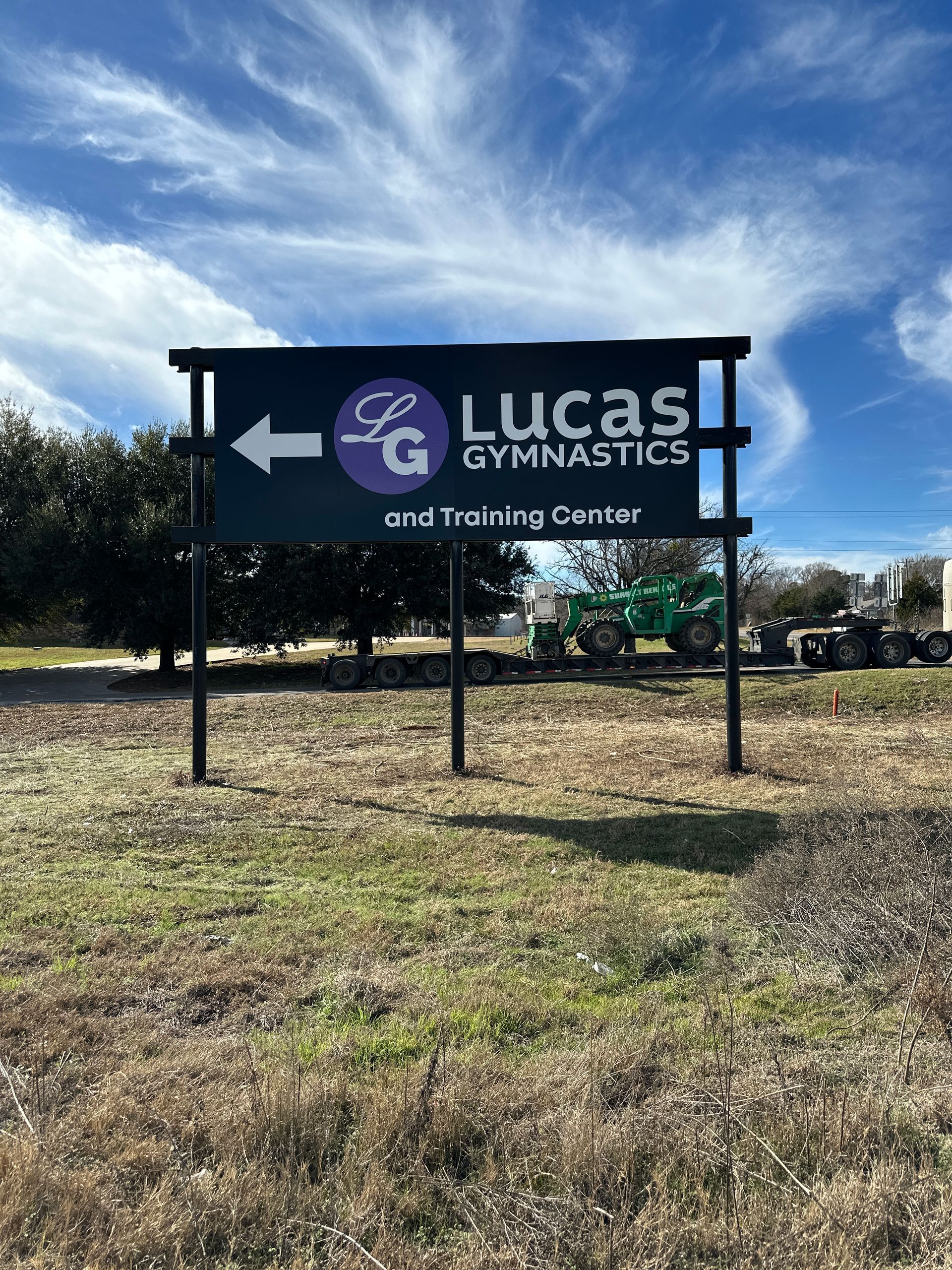 Lucas Gymnastics and Training Center sign on a grassy roadside under a blue sky.