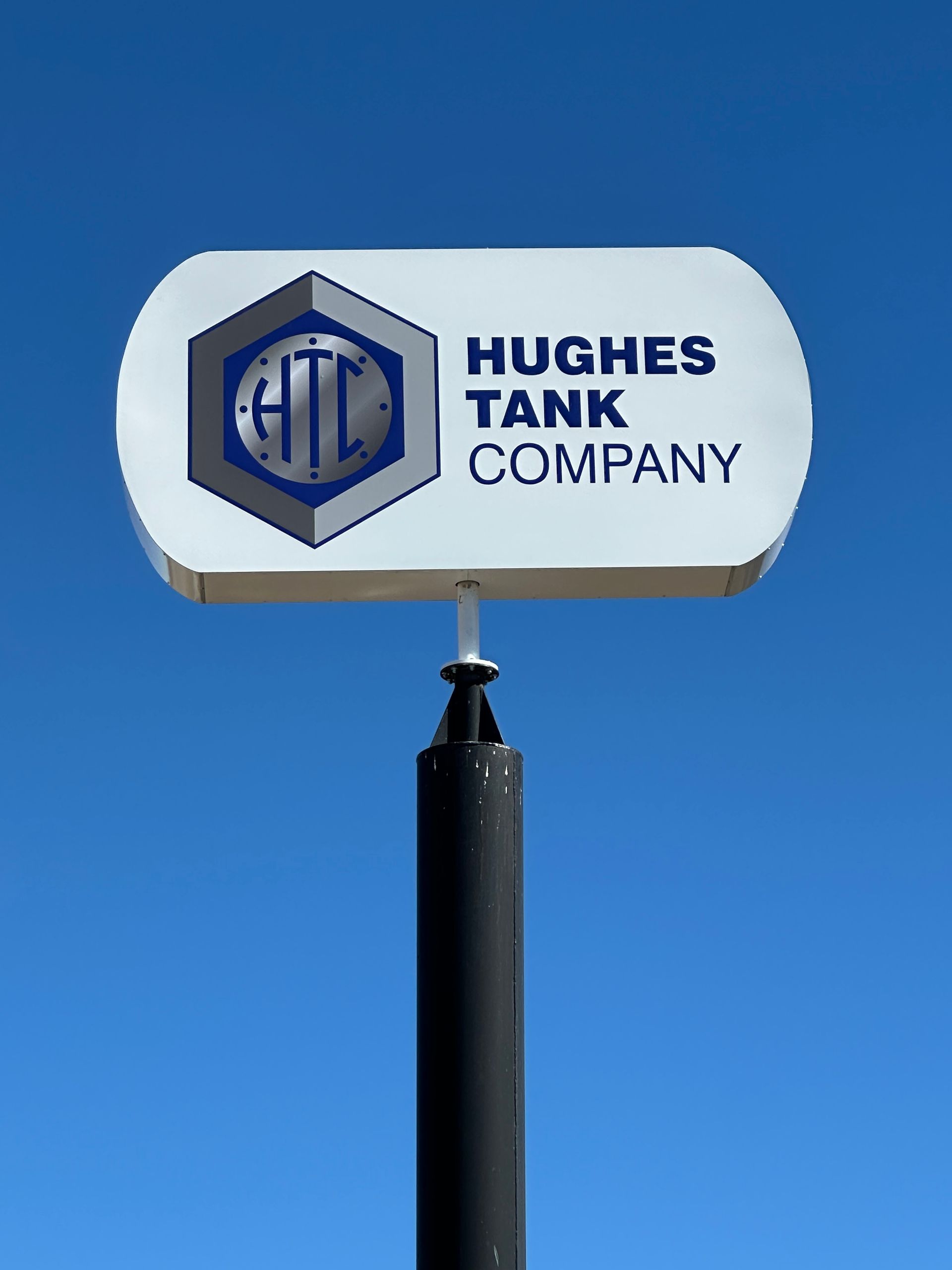 Hughes Tank Company sign on a pole against a blue sky