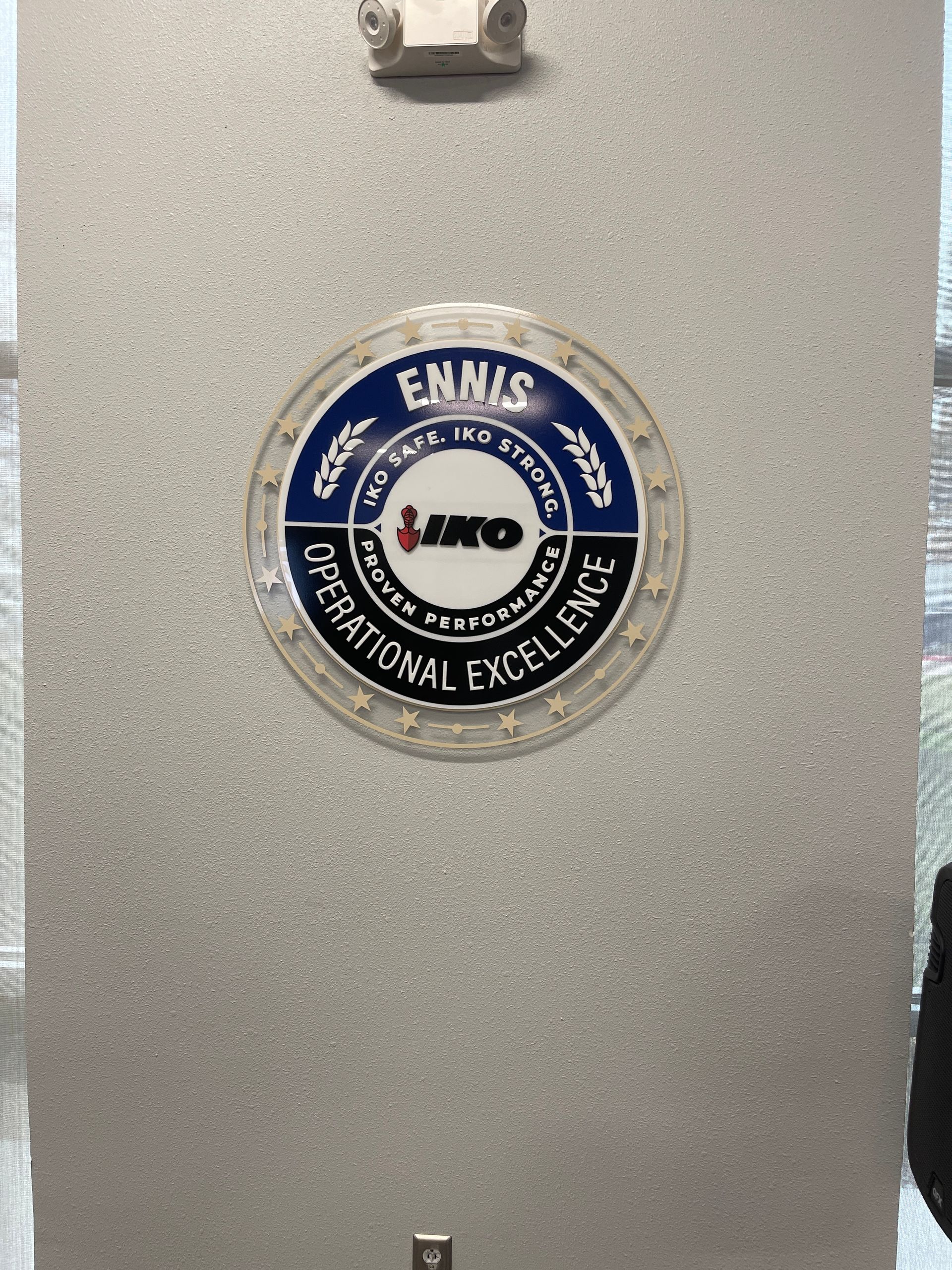 Round blue and white Ennis National Excellence award plaque on a textured gray wall
