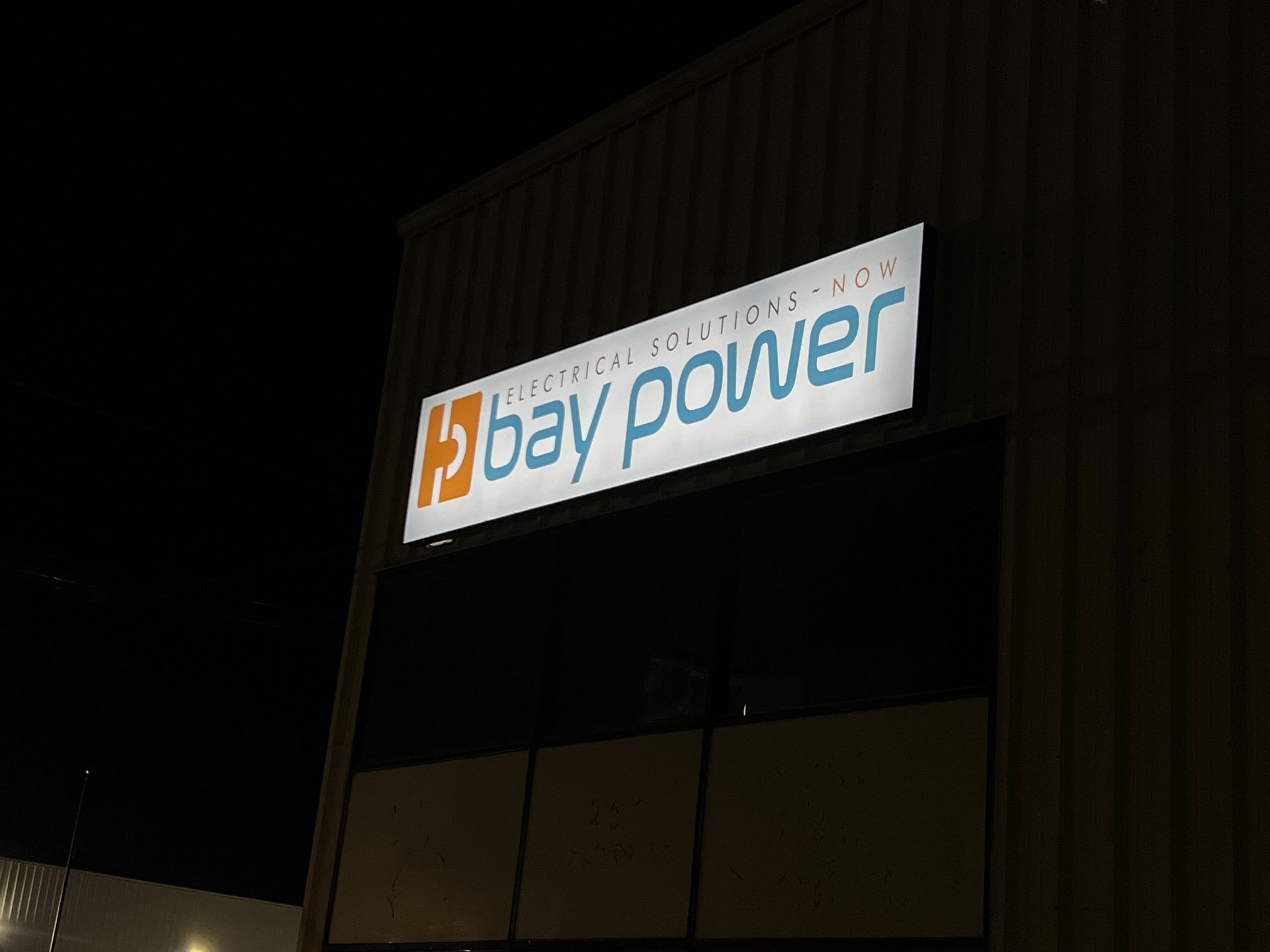 Nighttime exterior of a building with a lit “bay power” sign on the facade.
