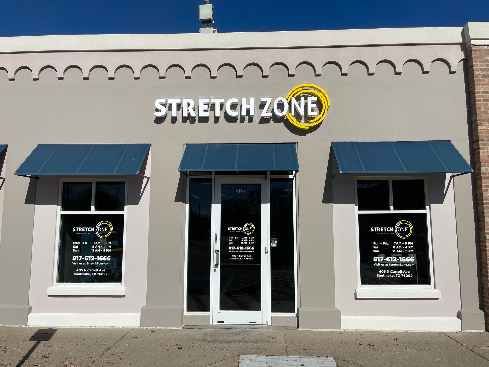 Storefront of Stretch Zone with blue awnings and glass entrance on a beige building