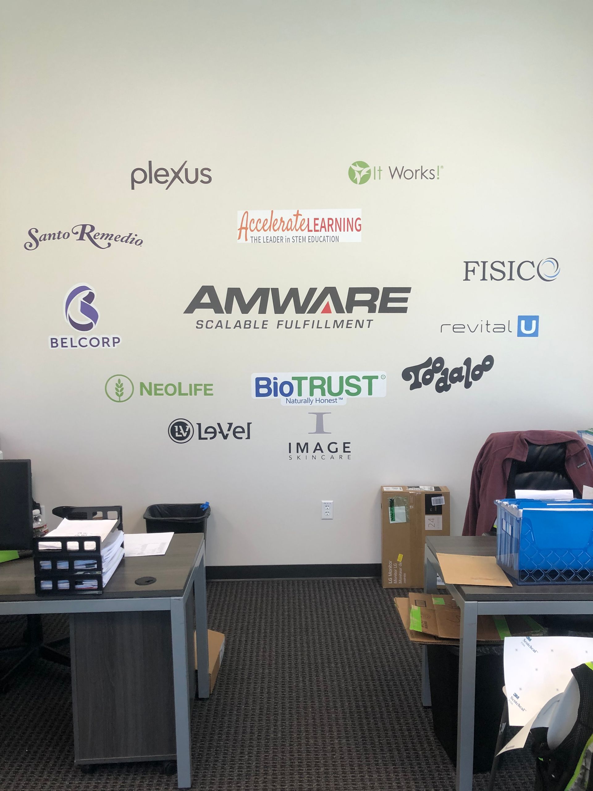 Lab lobby wall with company logos above desks, monitor, boxes, and a covered machine.