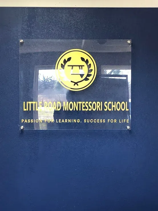 Little Dard Montessori School sign on a blue wall with yellow logo and text