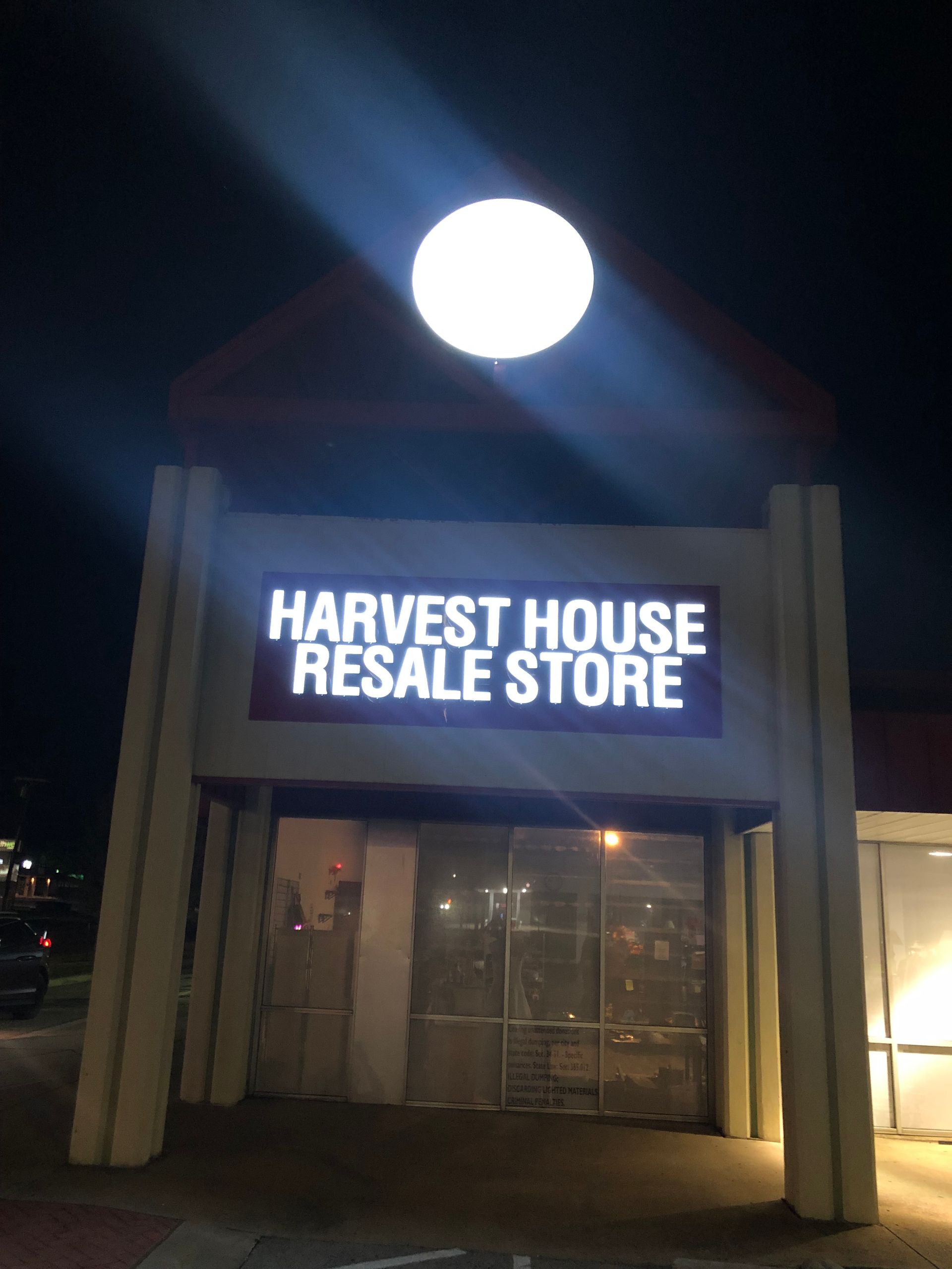 Harves t House Resale Store storefront at night with a bright round sign above the entrance