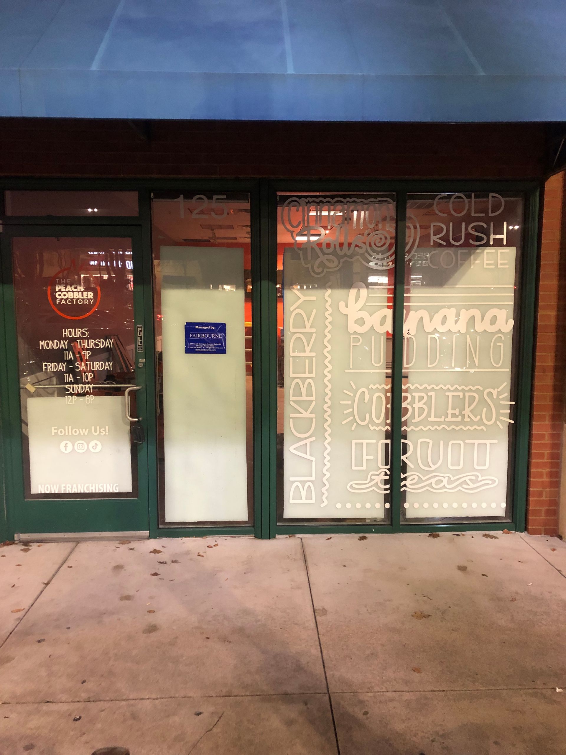 Green storefront with large front windows and a sidewalk outside at dusk