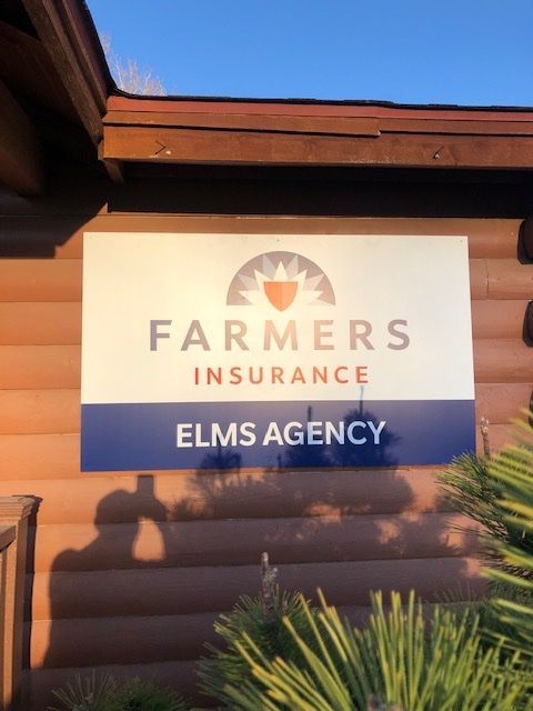Farmers Insurance Elms Agency sign on a log cabin exterior, lit by sunlight