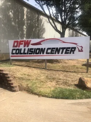 White banner sign reading “NEW COLLISION CENTER” in red and black beside a road and trees
