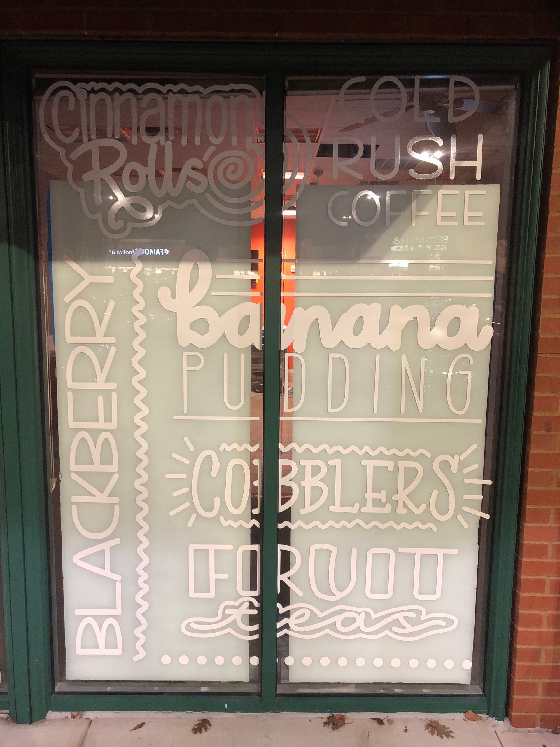 Chalkboard storefront menu listing cinnamon rolls, coffee, bananas, cobblers and fruit, in white and orange lettering