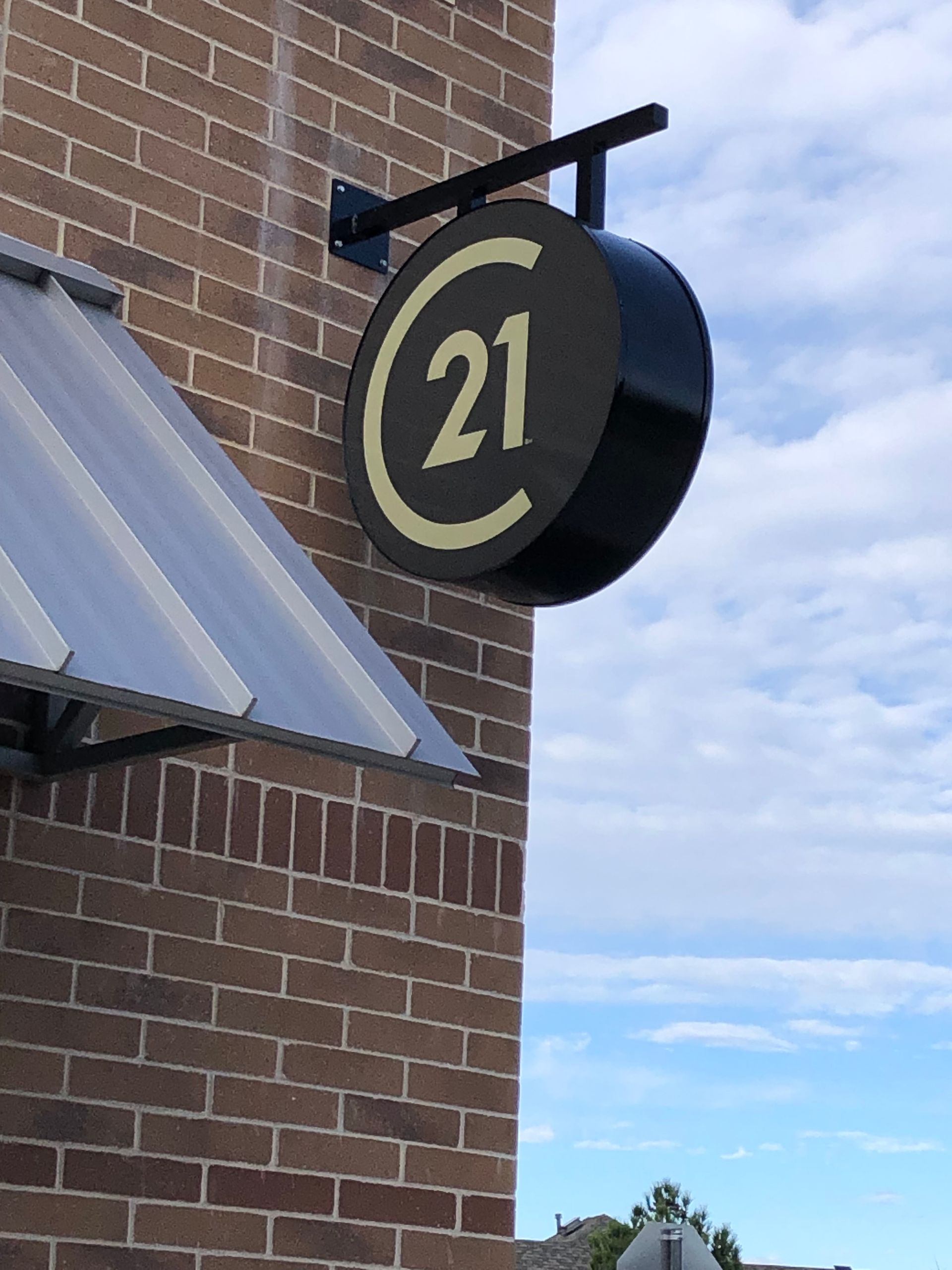 Black round sign with gold “21” mounted on a brick building against a blue sky.