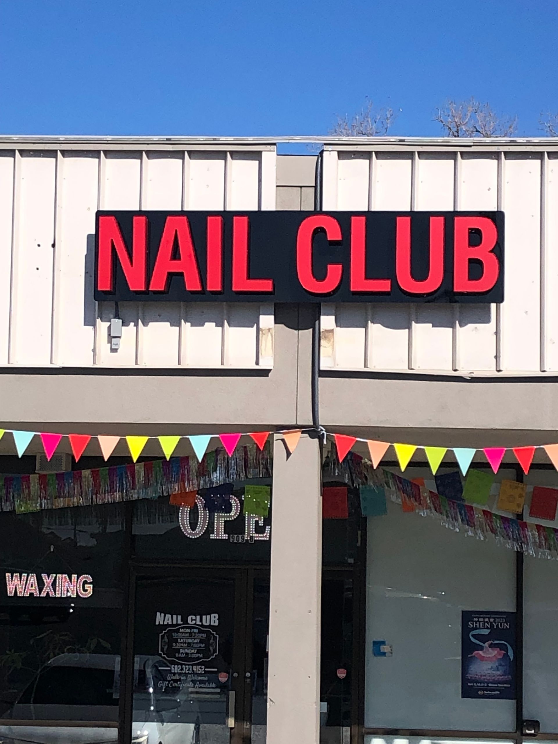 Storefront sign reading “NAIL CLUB” in red letters above a shop with colorful pennant flags.
