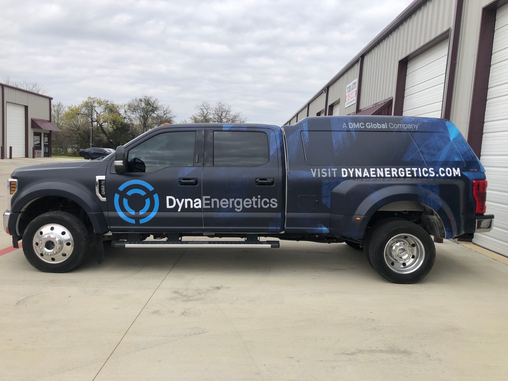 DynEnergetics-branded black pickup truck parked outside warehouse buildings