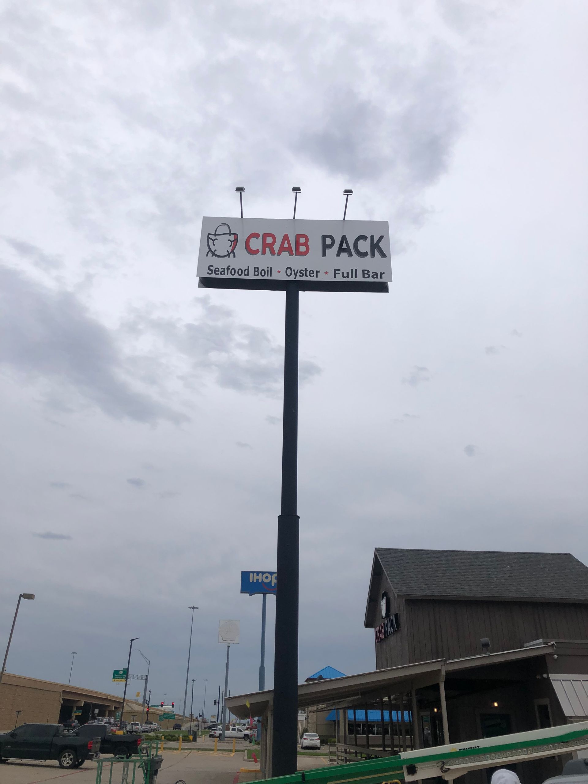 Crab Pack roadside sign on a tall pole by a building under a cloudy sky