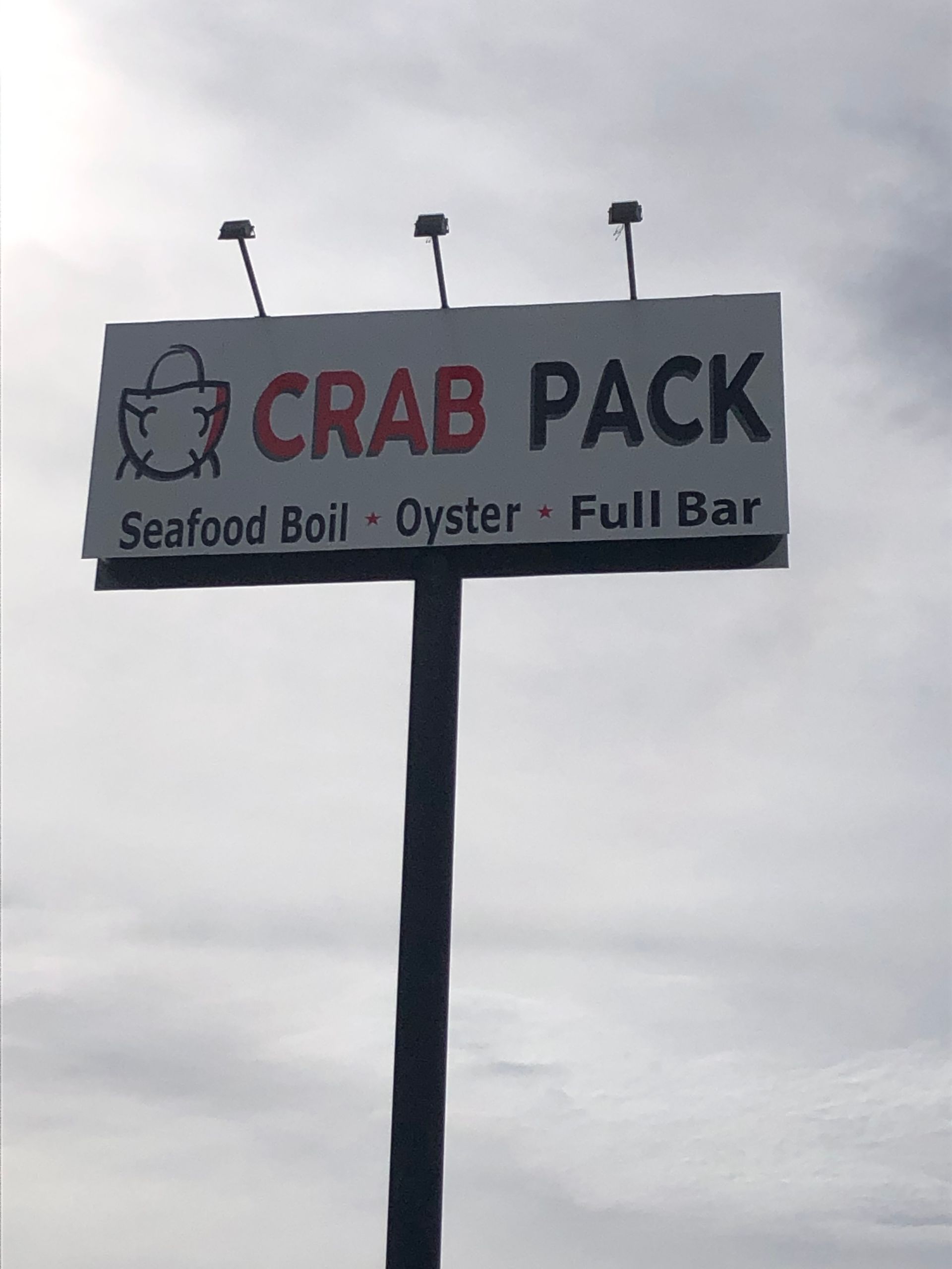 Crab Pack seafood bar sign on a pole against a cloudy sky.