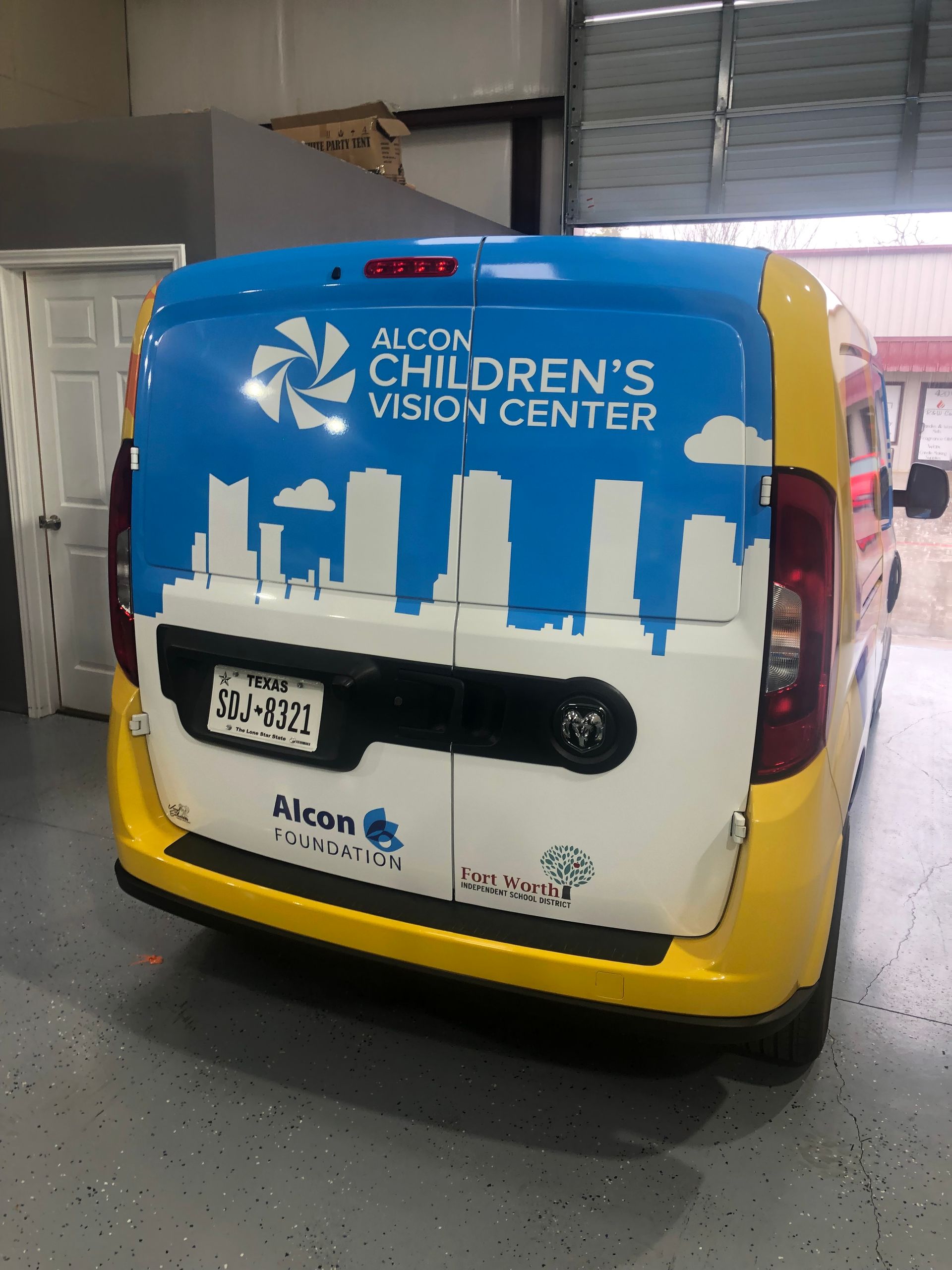 Blue-and-white van for Alabama Children’s Vision Center parked indoors with city skyline graphic.