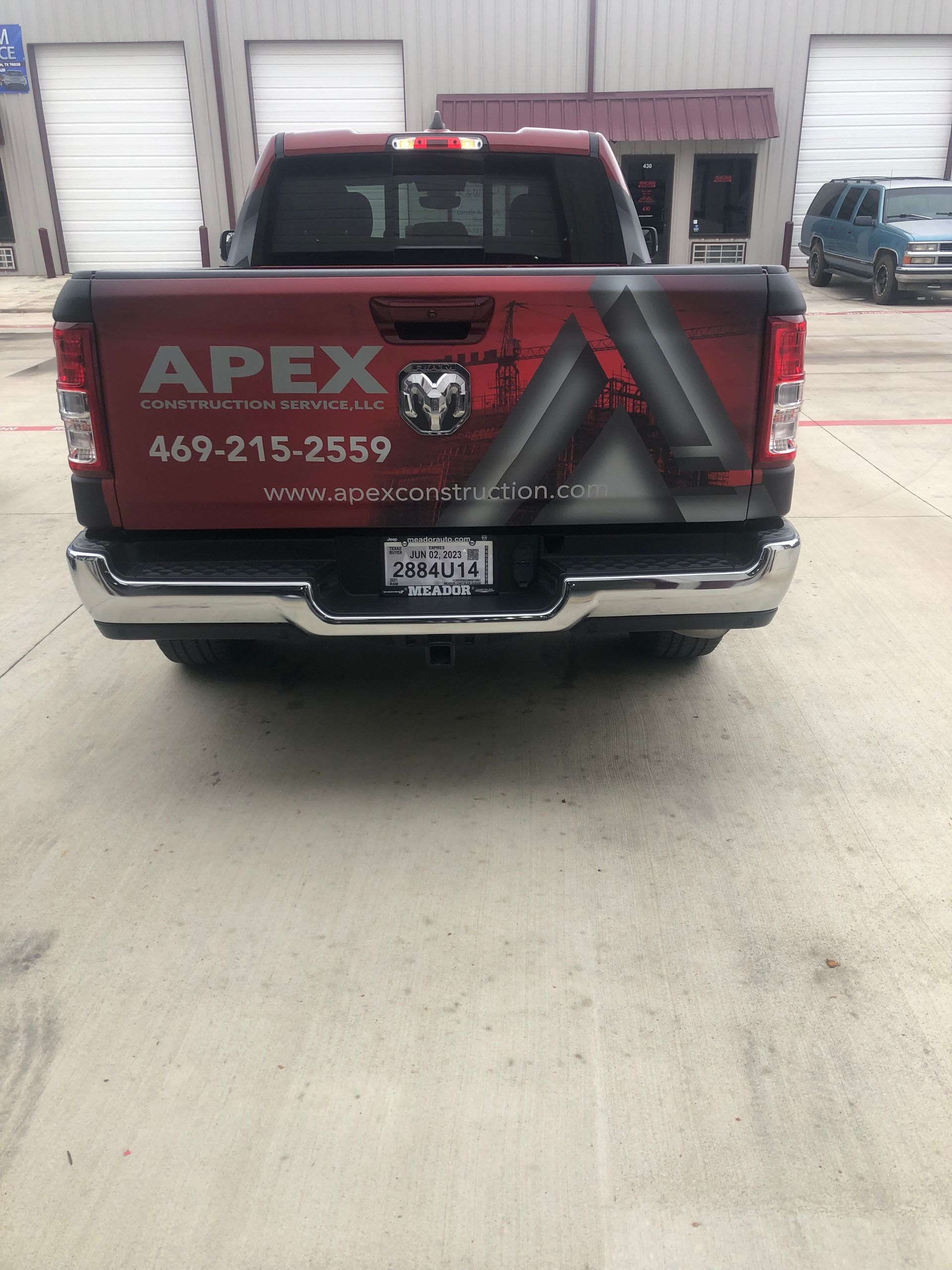 Red APEX pickup truck with company logo and phone number parked outside warehouse doors