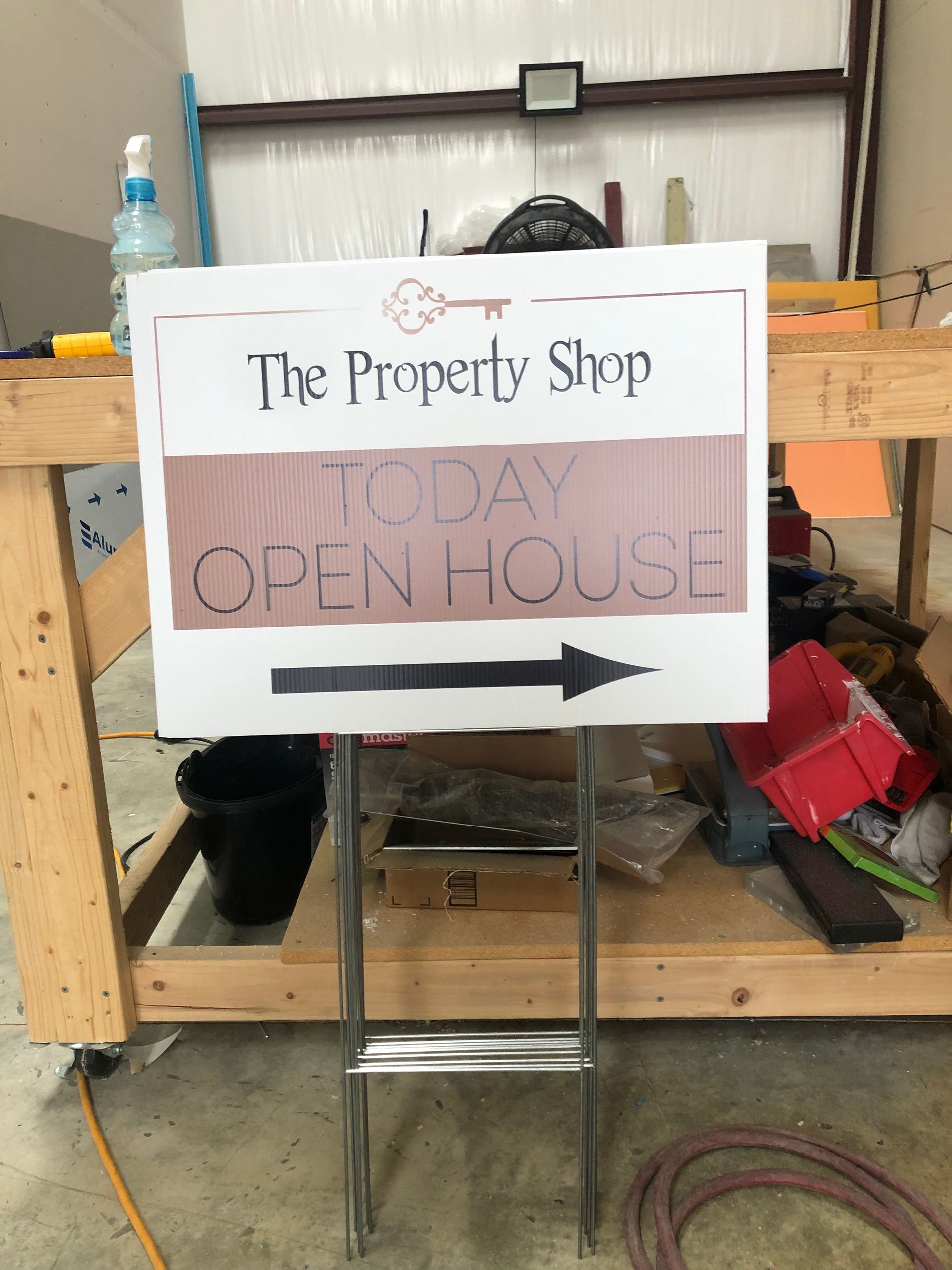 Sign for “The Property Shop” saying “Today Open House” with a right-pointing arrow, on a stand indoors