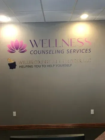 Wellness Counseling Services wall sign with pink lotus logo in a gray office lobby