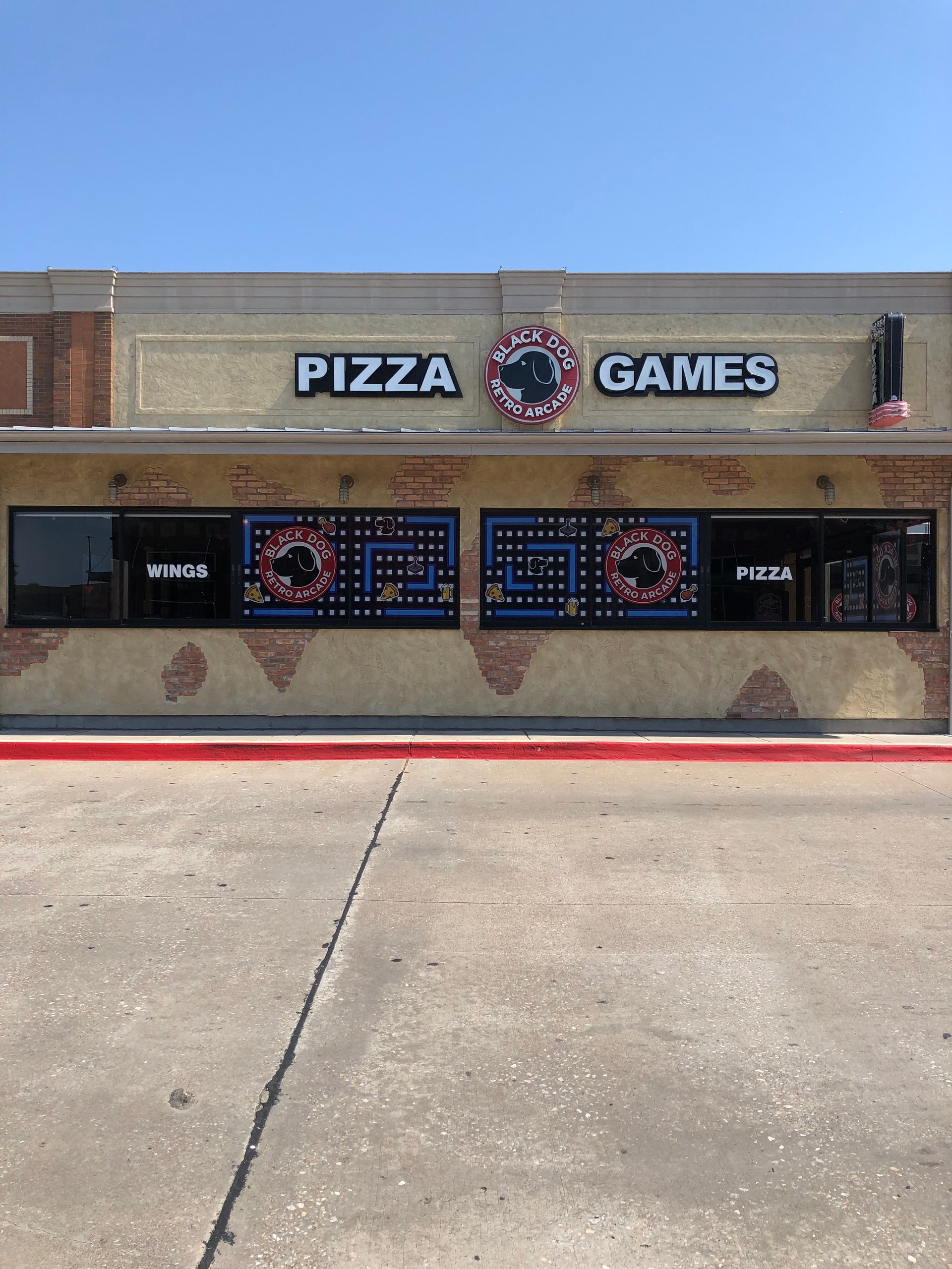 Pizza and games storefront with brick facade, neon signs, and blue sky overhead