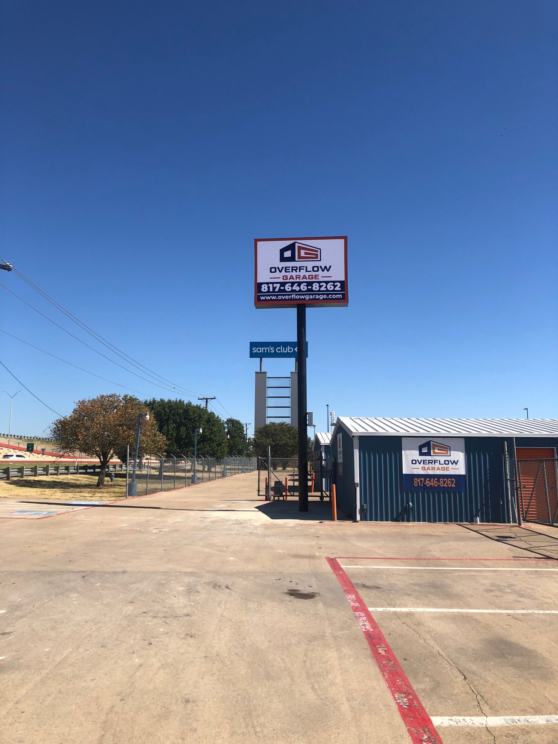 Outdoor storefront with a tall sign, blue shipping container, and clear blue sky over a paved lot.