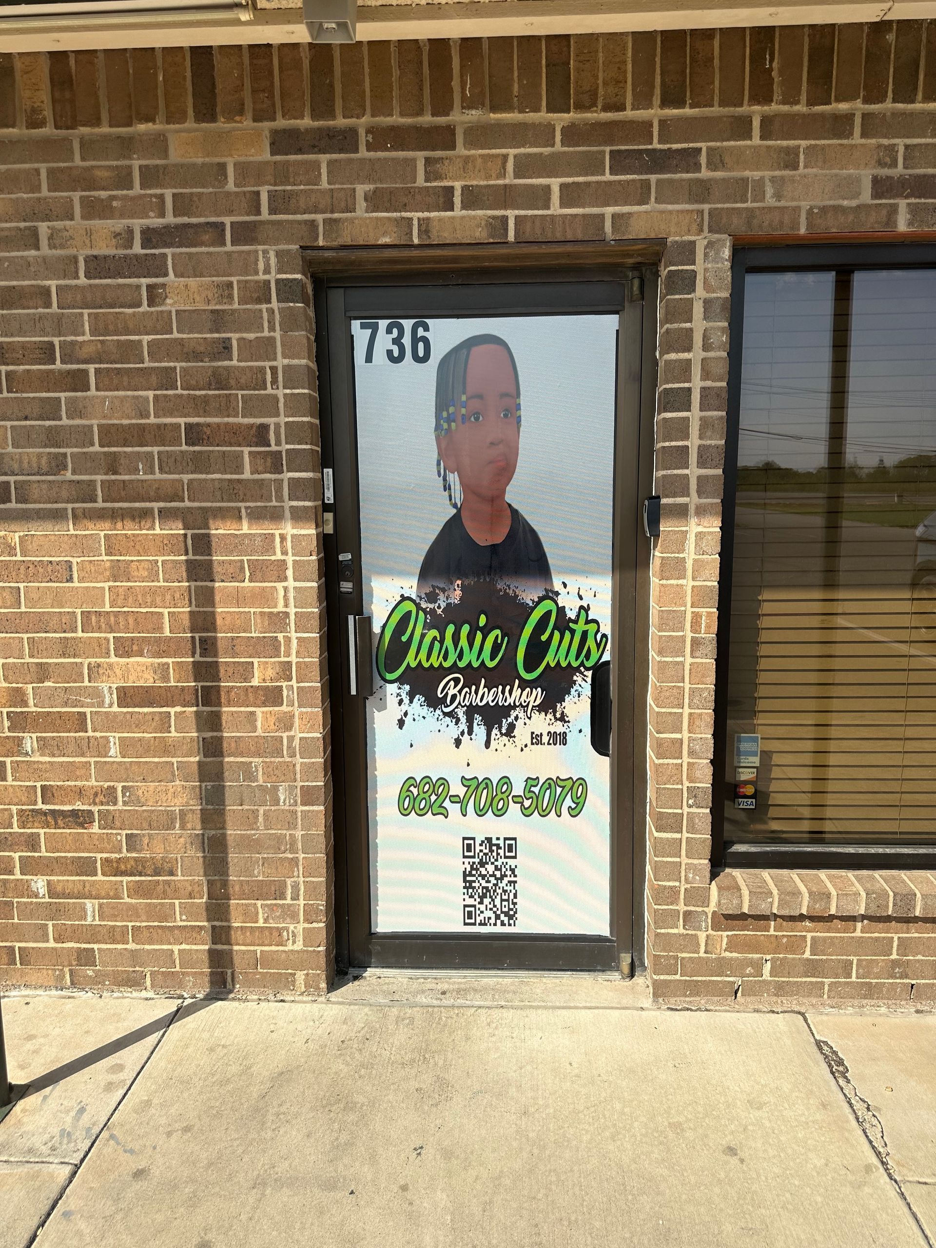 Storefront door with a large promotional poster and QR code on a brick building.