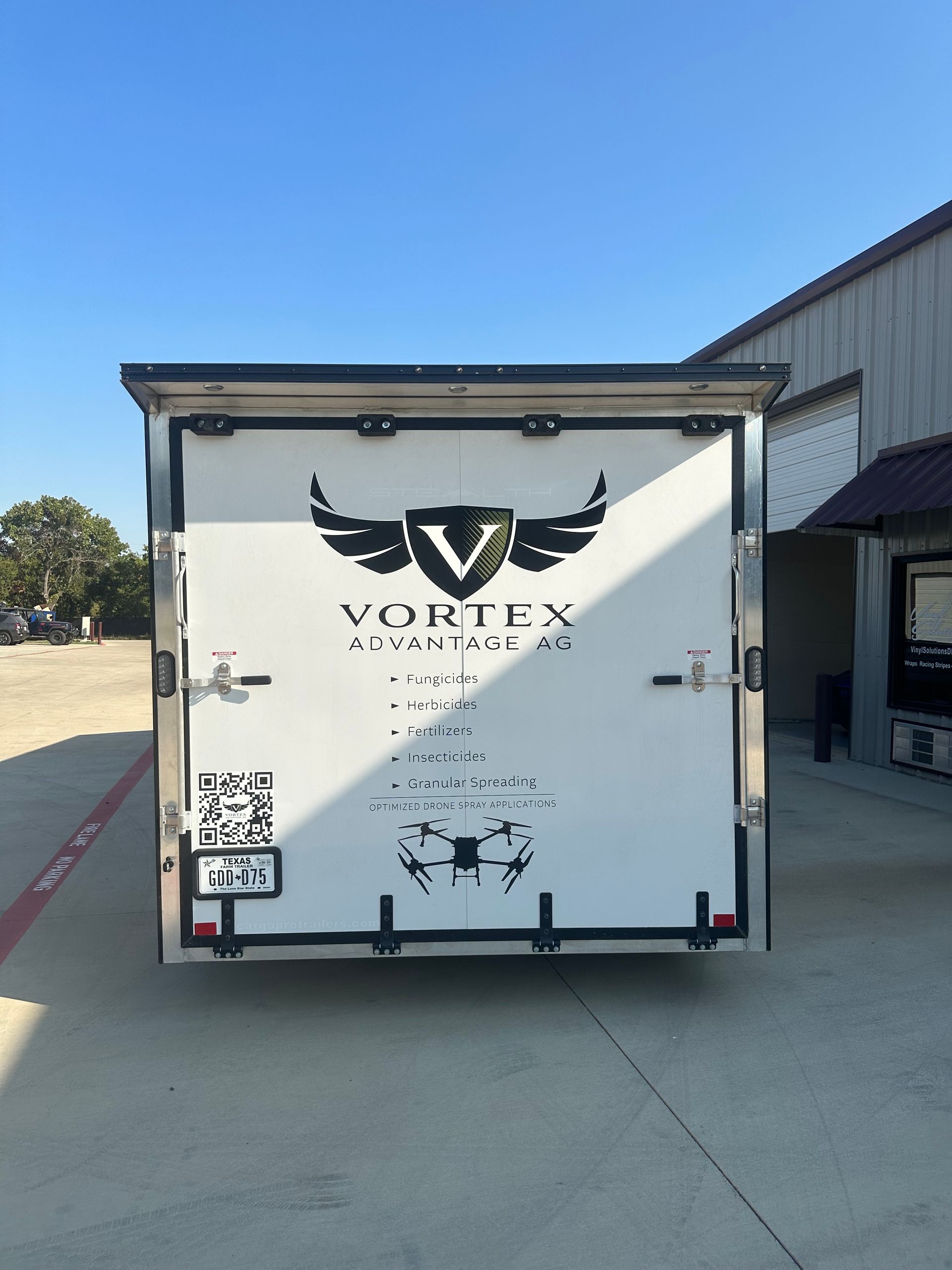 White Vortex-branded trailer parked beside a warehouse on a sunny day.