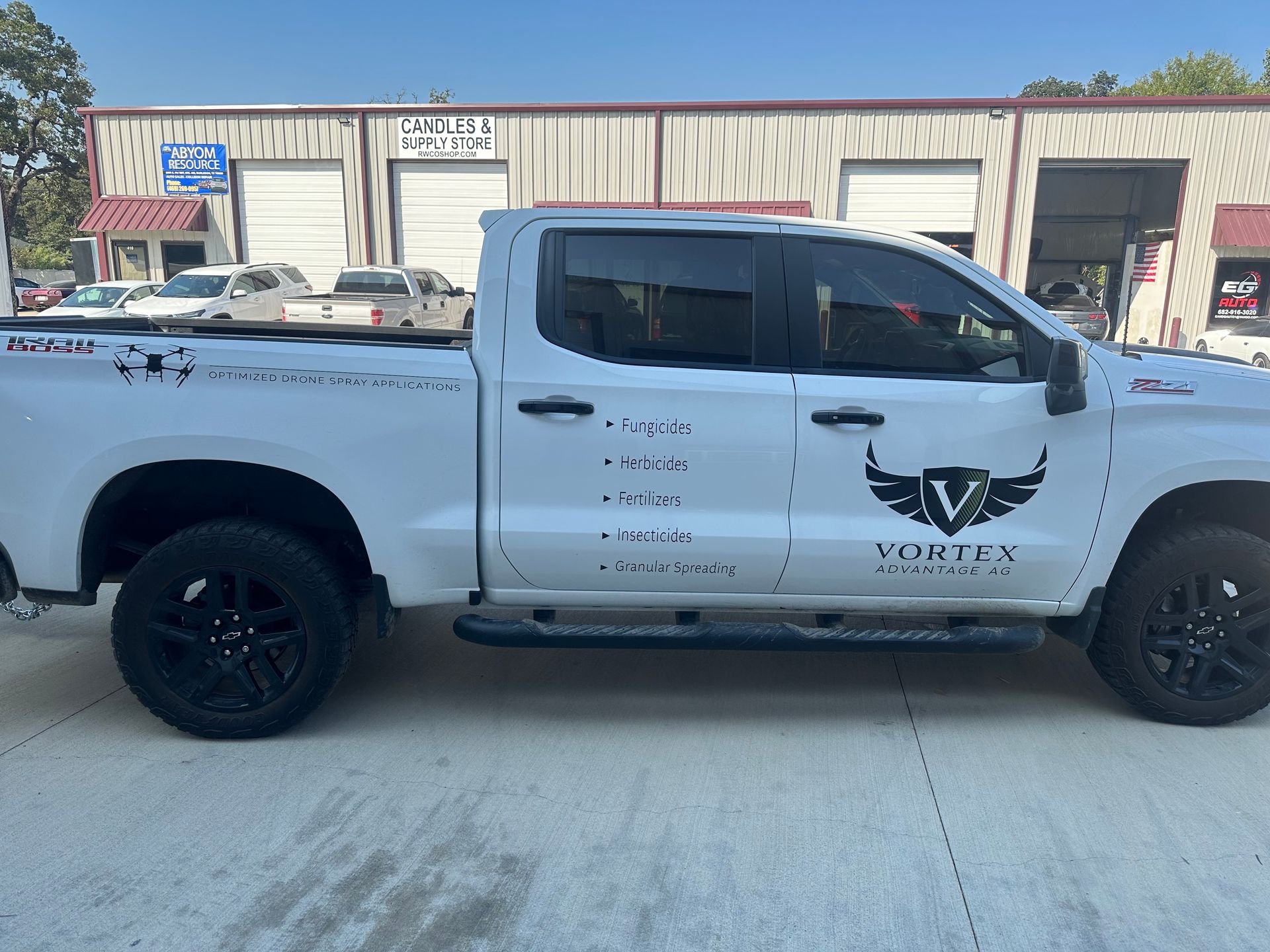 White pickup truck with black wheels parked in front of a commercial building.