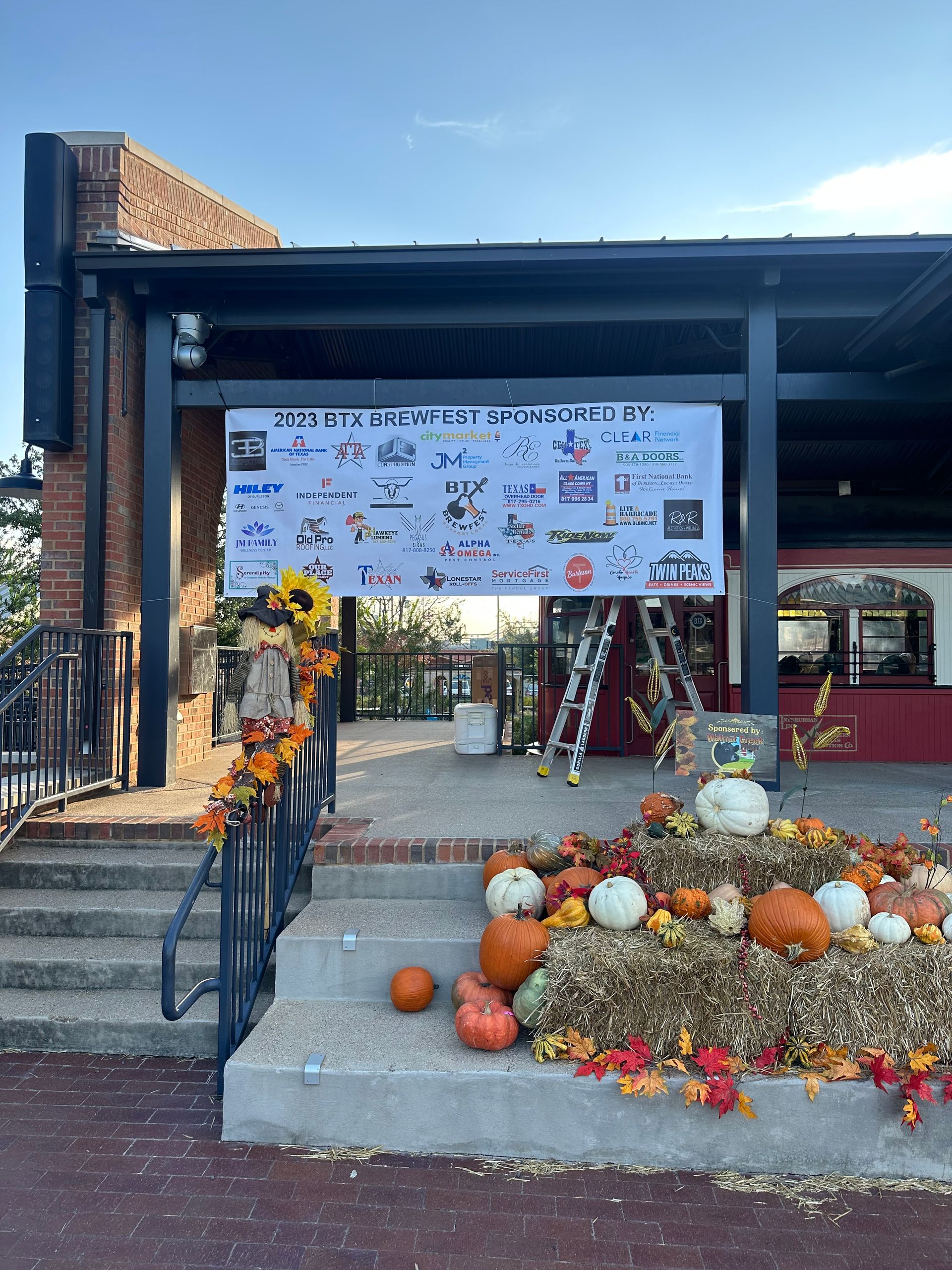 Fall-themed entry with pumpkins and mums beneath a banner under a covered walkway