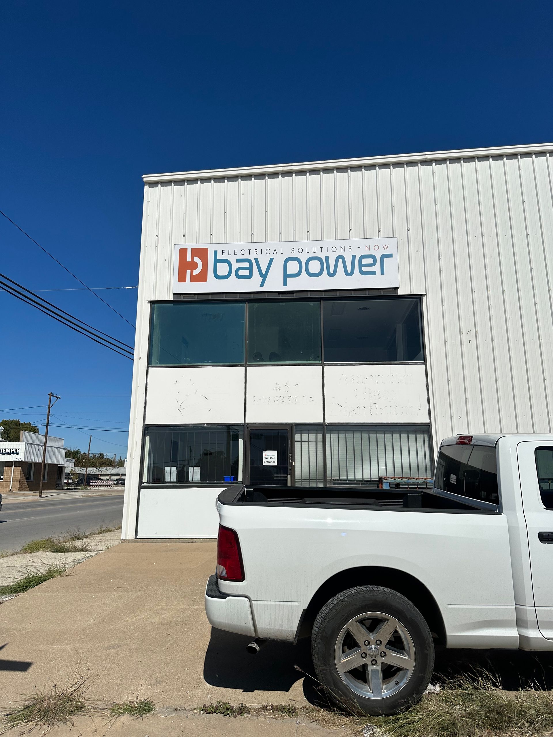 White pickup truck parked outside a Bay Power building under a clear blue sky.