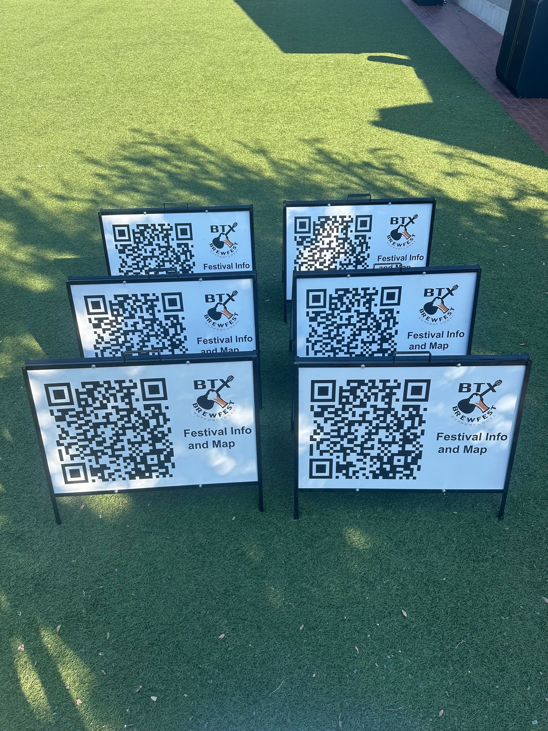 Six QR code signs on stakes arranged on green grass in bright sunlight