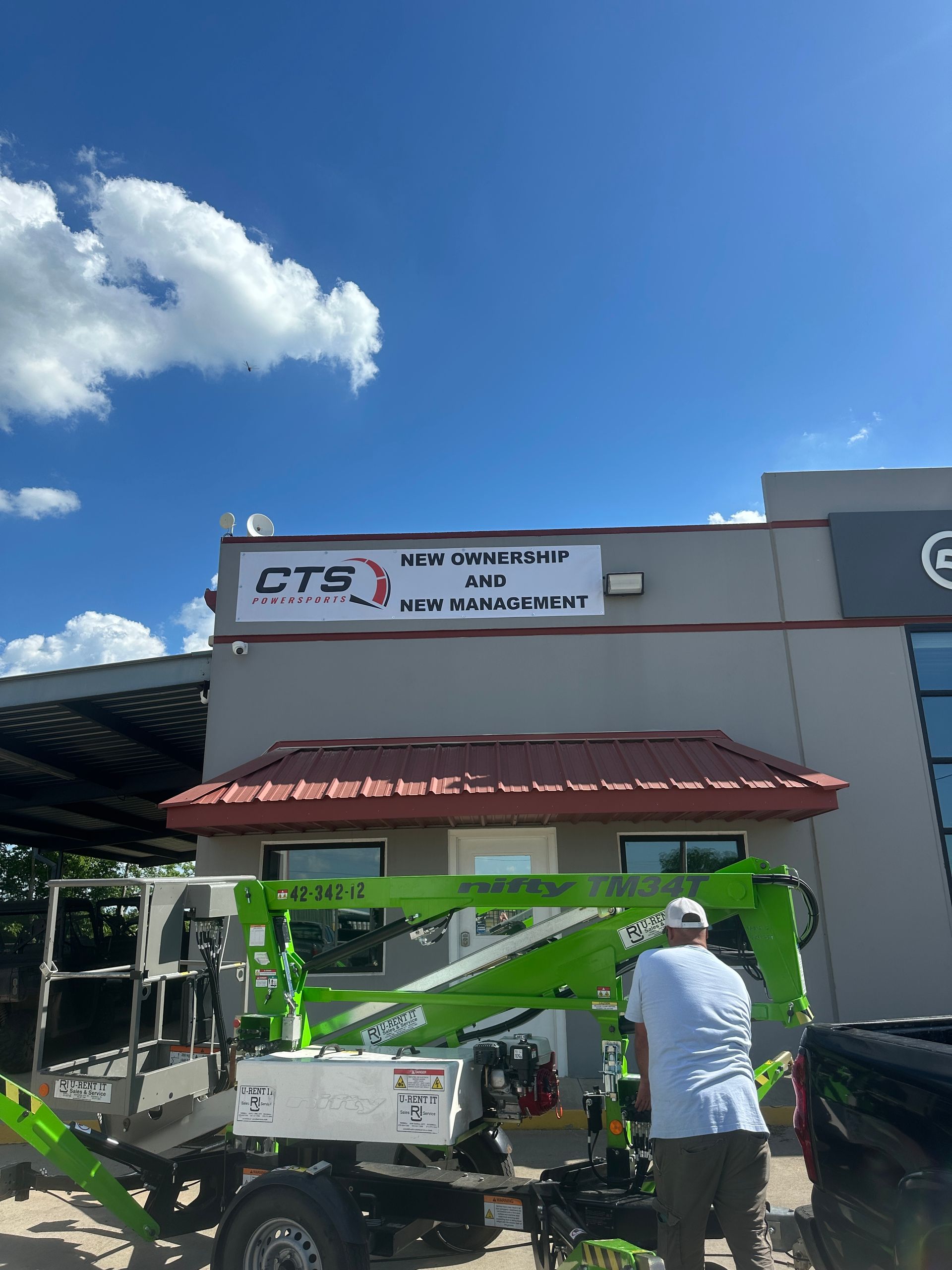 Two people working near a green utility truck outside a building with a CTS sign under a blue sky